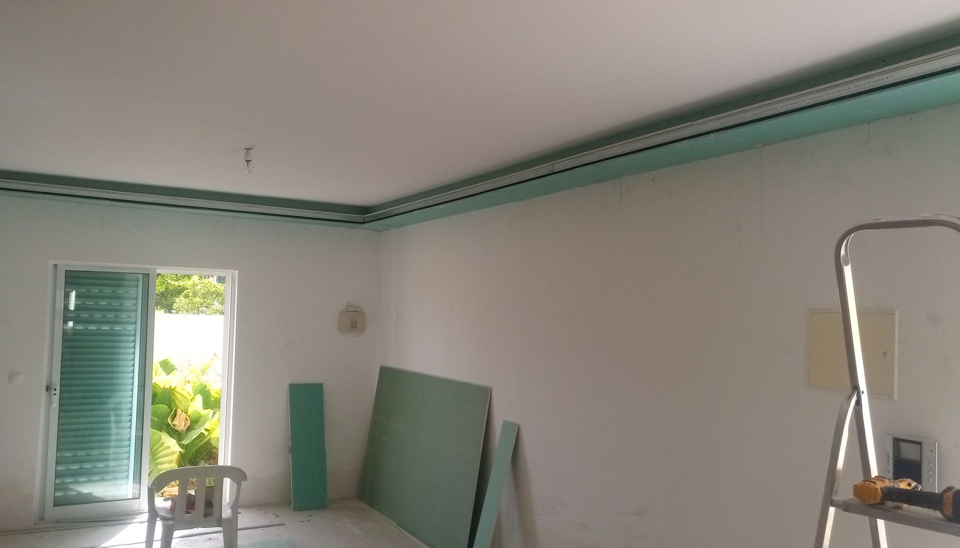 Quarto em construção; paredes brancas, detalhes em turquesa, teto inacabado, porta verde, escada.