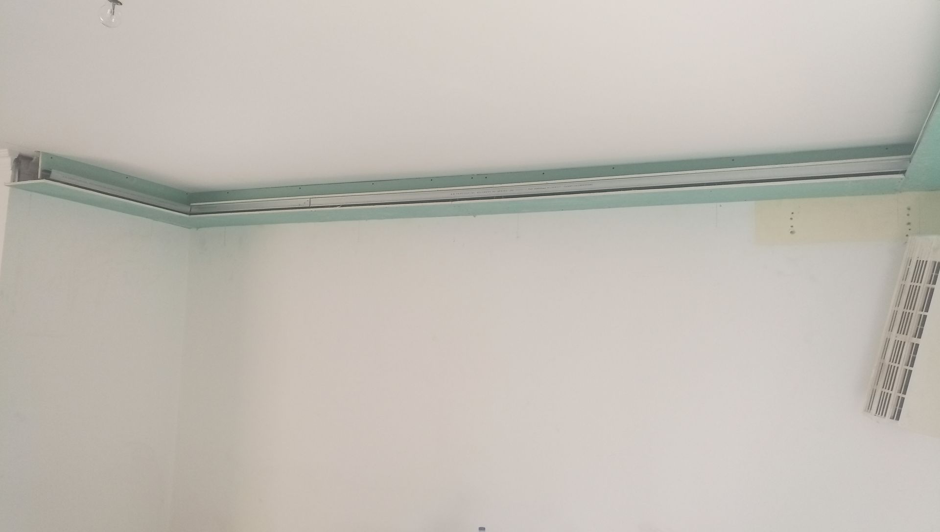 Um canto da sala com uma canaleta para cabos verde-clara instalada ao longo da parte superior das paredes brancas.