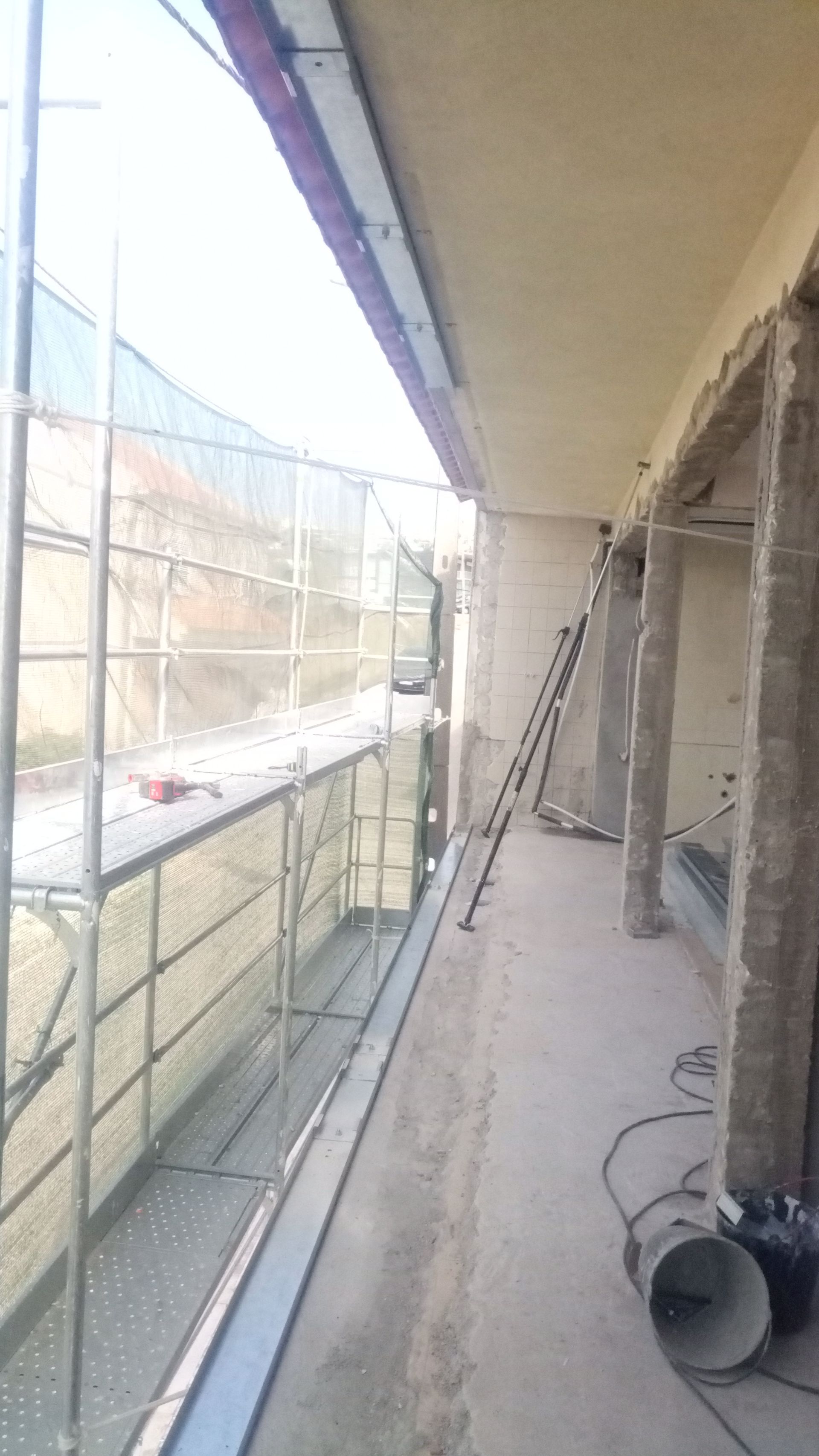 Andaimes montados ao lado da varanda de um prédio durante a construção; uma escada encostada na parede.