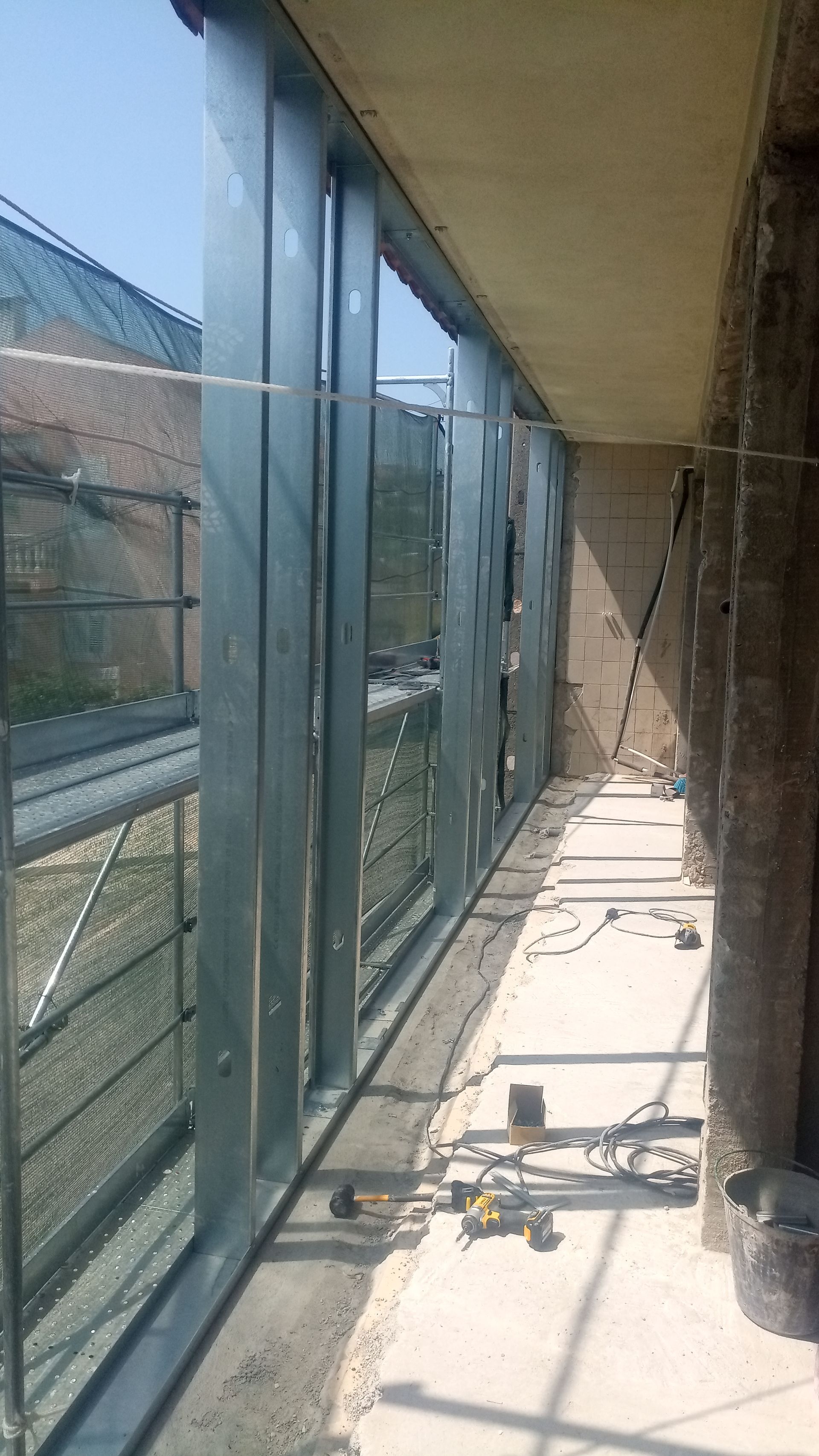 Canteiro de obras com estrutura metálica. Varanda longa e estreita. Muita luz natural.