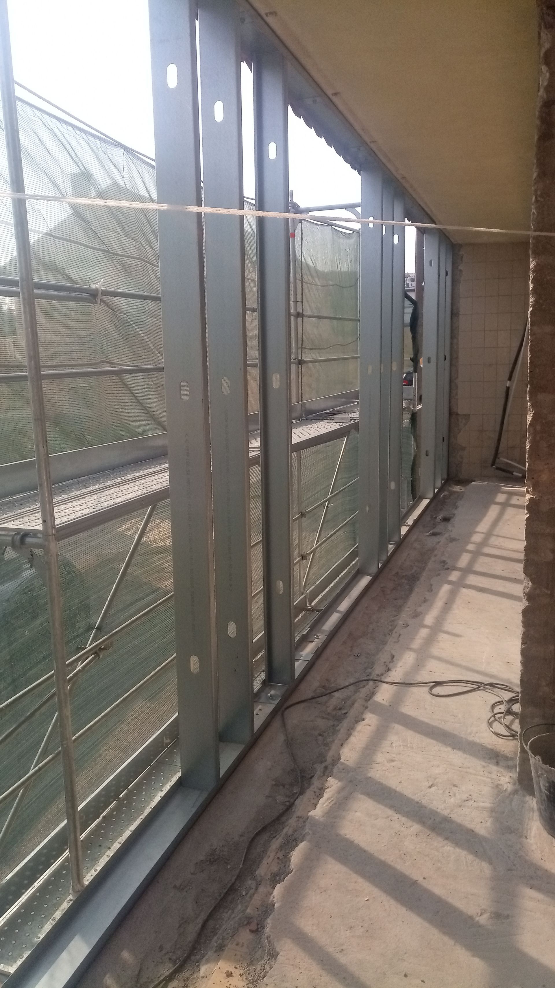 Estrutura metálica para parede externa de uma varanda, com tela metálica e piso de concreto.
