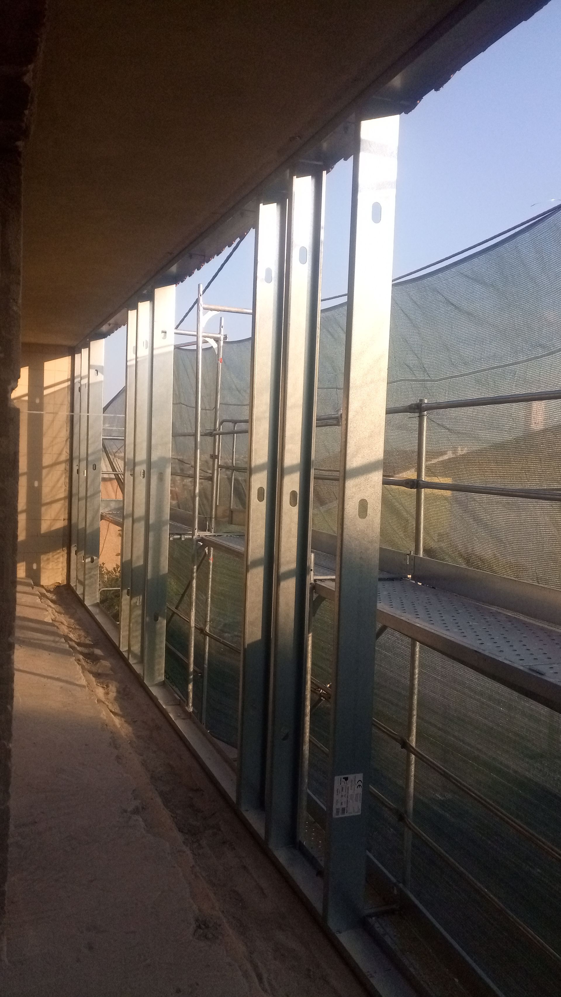 Varanda com estrutura metálica e rede de proteção, sob um céu ensolarado.