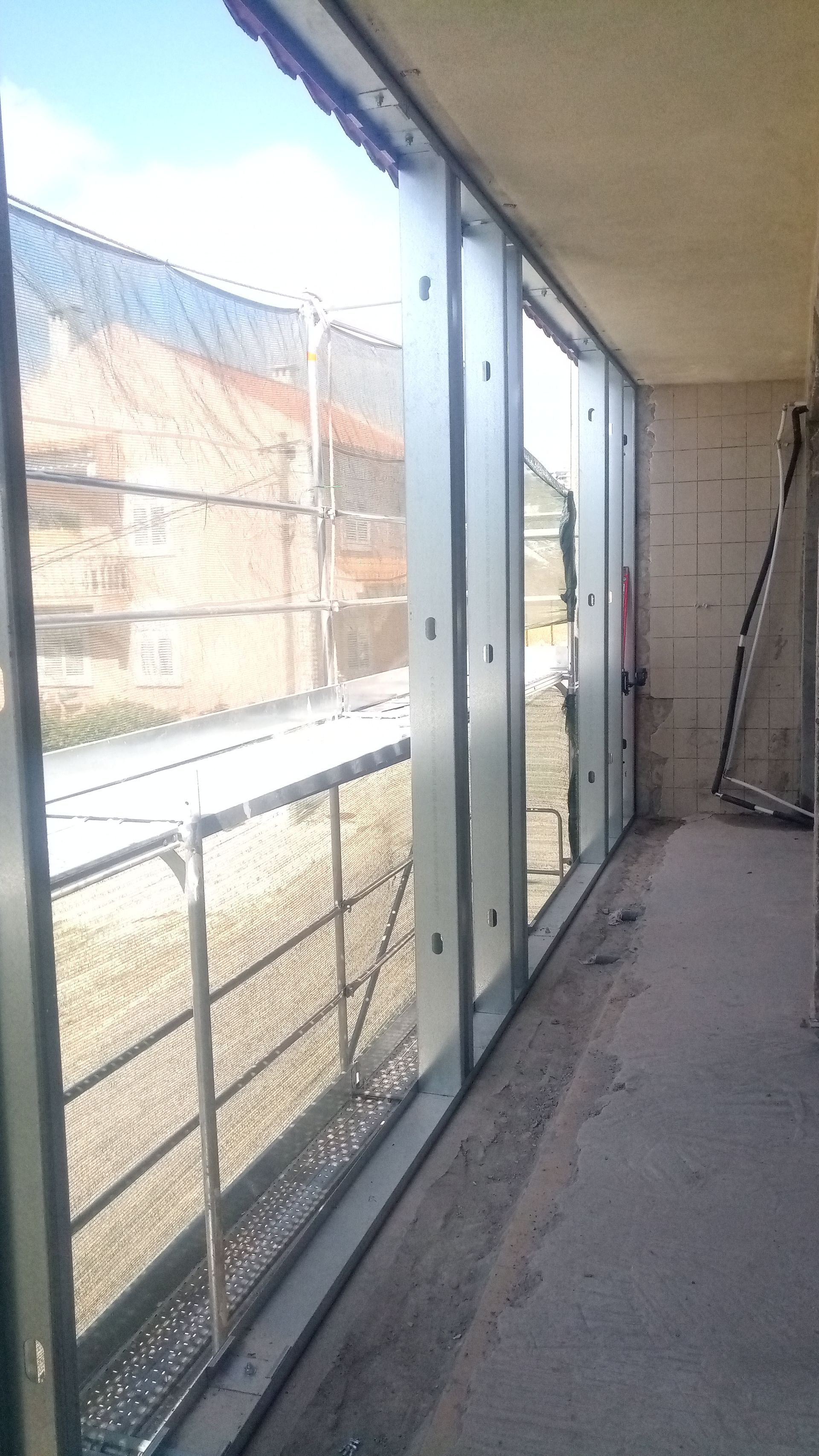Um cômodo parcialmente construído com uma grande janela com vista para a rua e para os prédios.