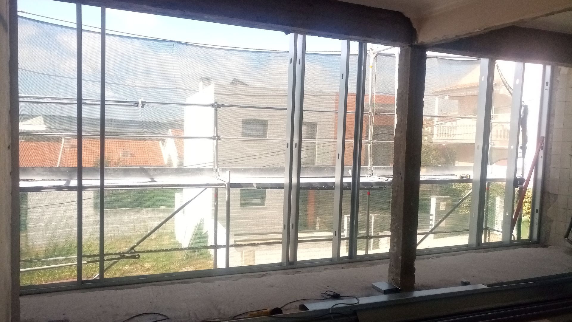 Grandes janelas com molduras metálicas oferecem vista para edifícios e para o telhado, além do interior de um cômodo.