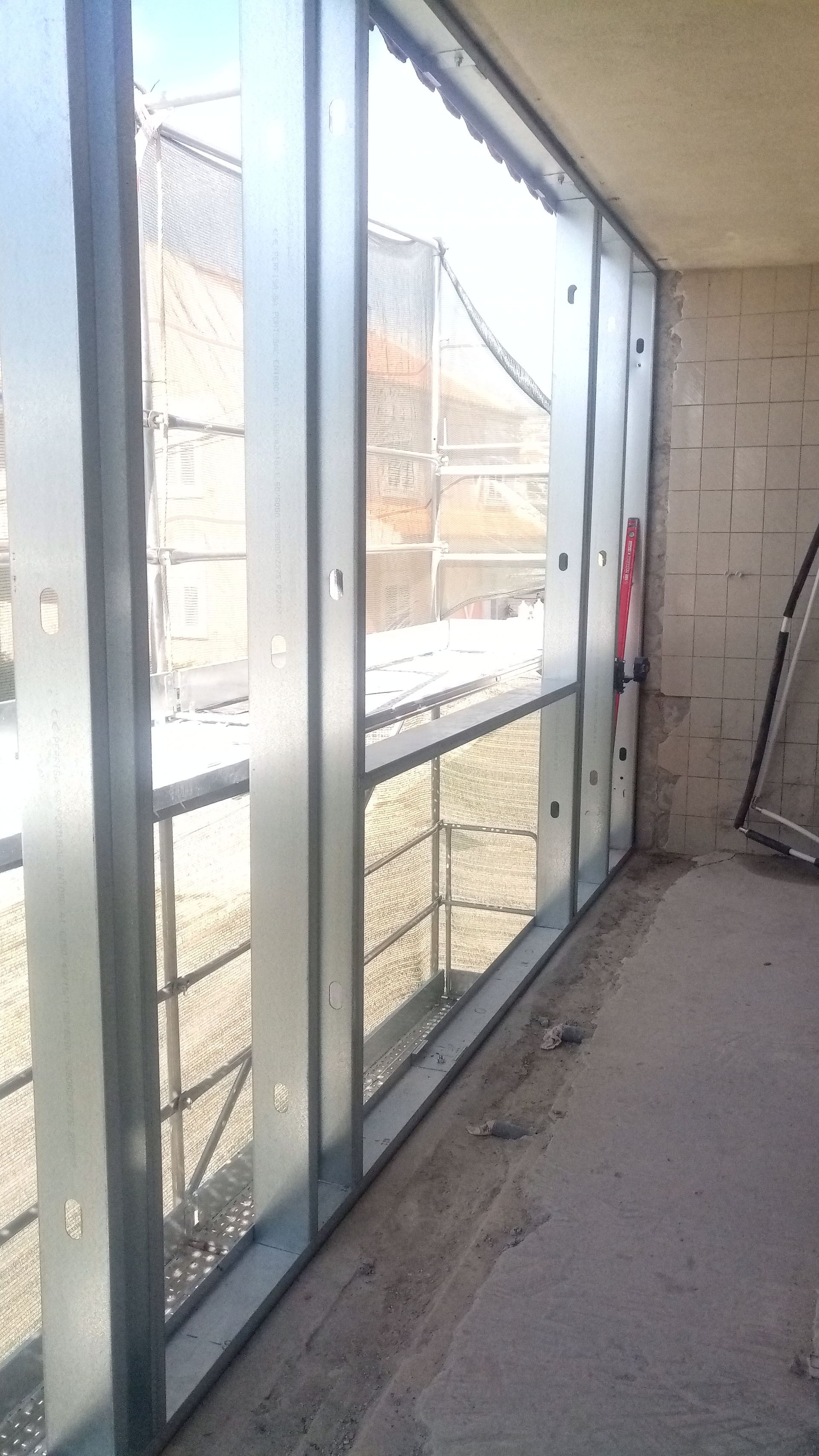 Janela com estrutura metálica em um canteiro de obras com andaimes visíveis e paredes inacabadas.