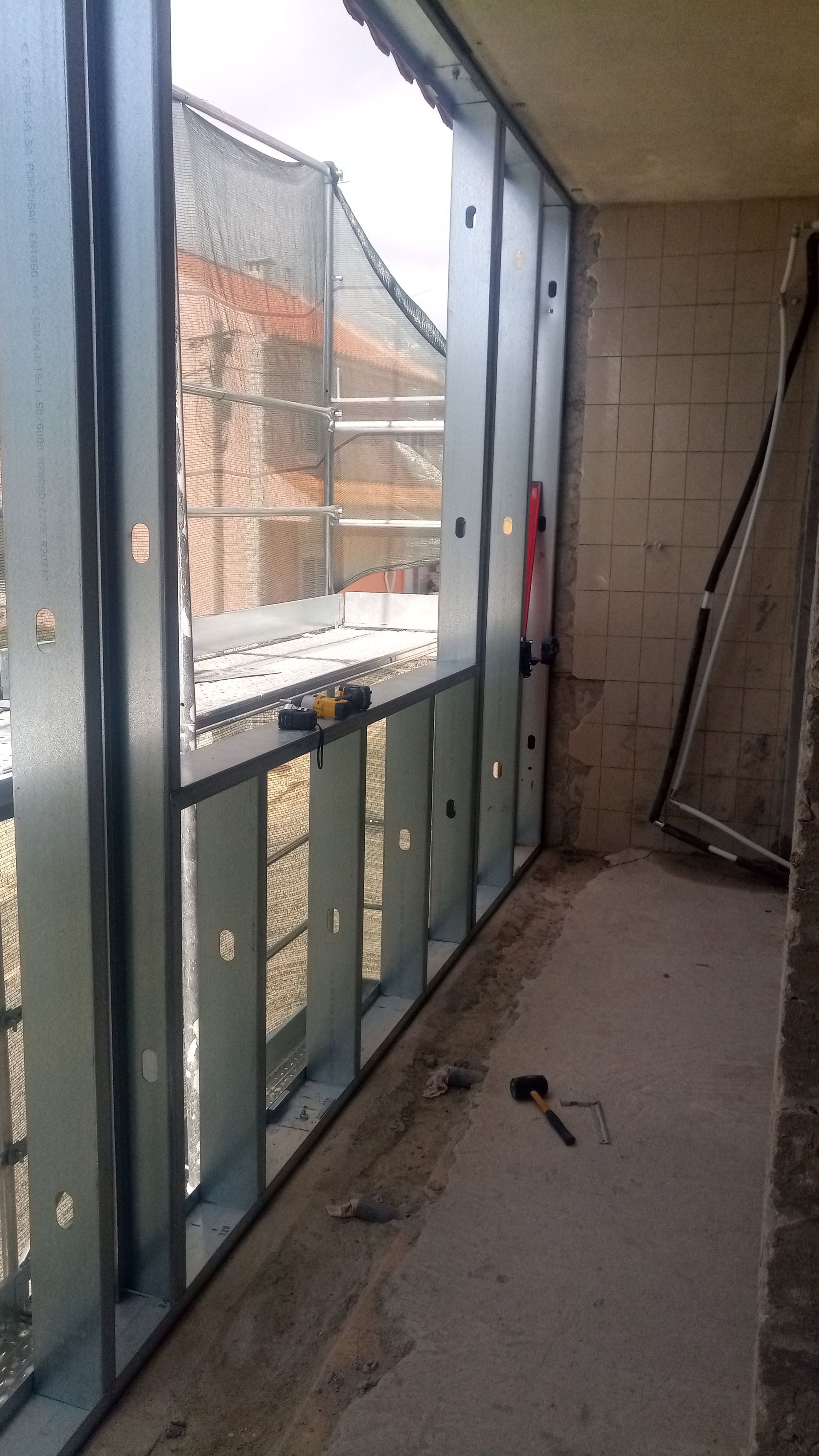Estrutura metálica de uma janela em um prédio em construção, com vista para o exterior.