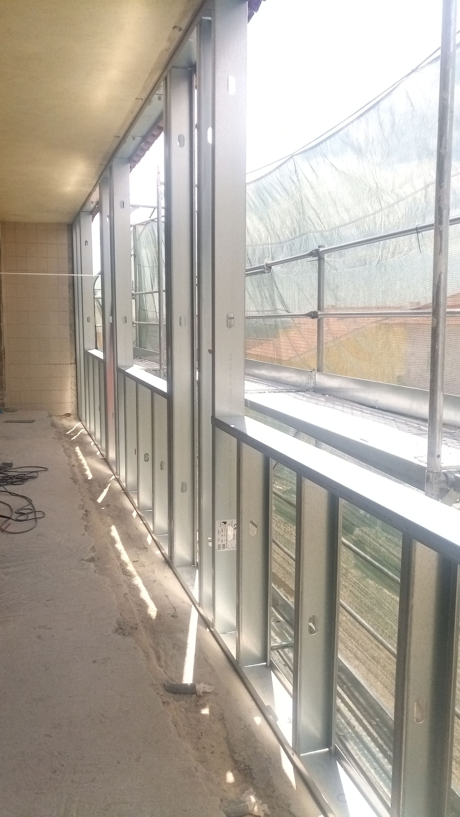 Estrutura metálica para janelas e guarda-corpo, com vista para cerca e árvores.