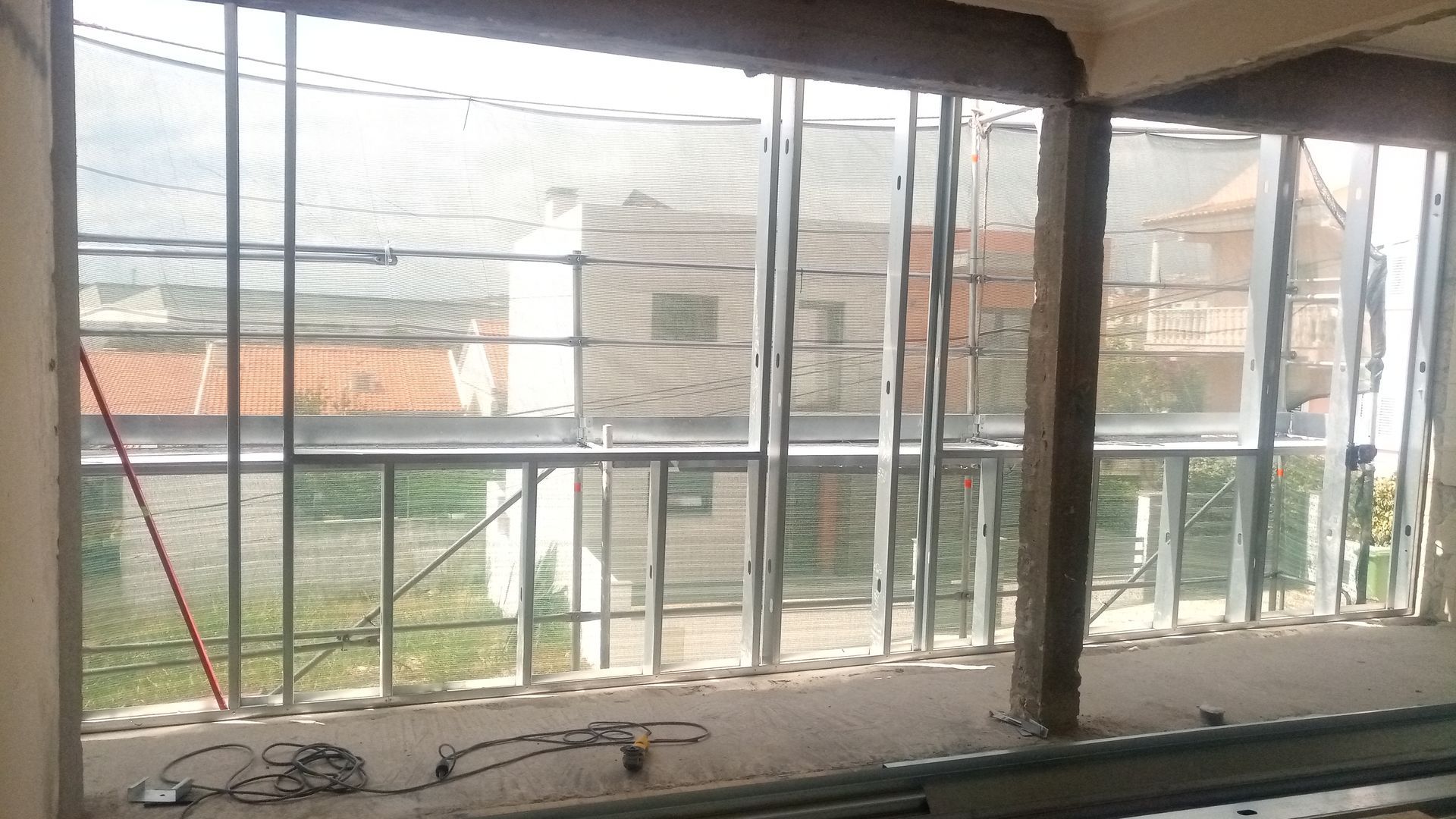 Vista interna de um edifício com uma grande janela. É possível ver os painéis de vidro, a estrutura metálica e os edifícios externos.