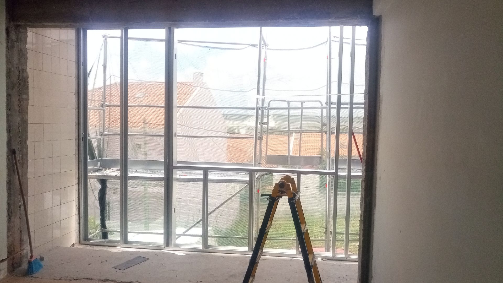 Vista interior de um edifício em construção, com as molduras das janelas e a paisagem urbana visível através da abertura.