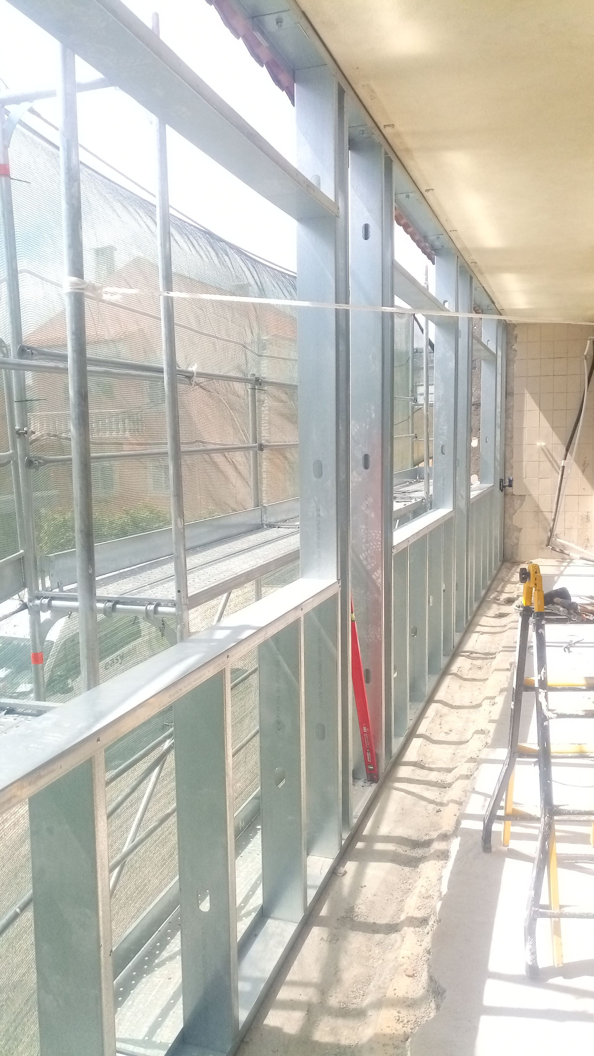 Estrutura metálica de uma parede com aberturas para janelas, em um canteiro de obras.