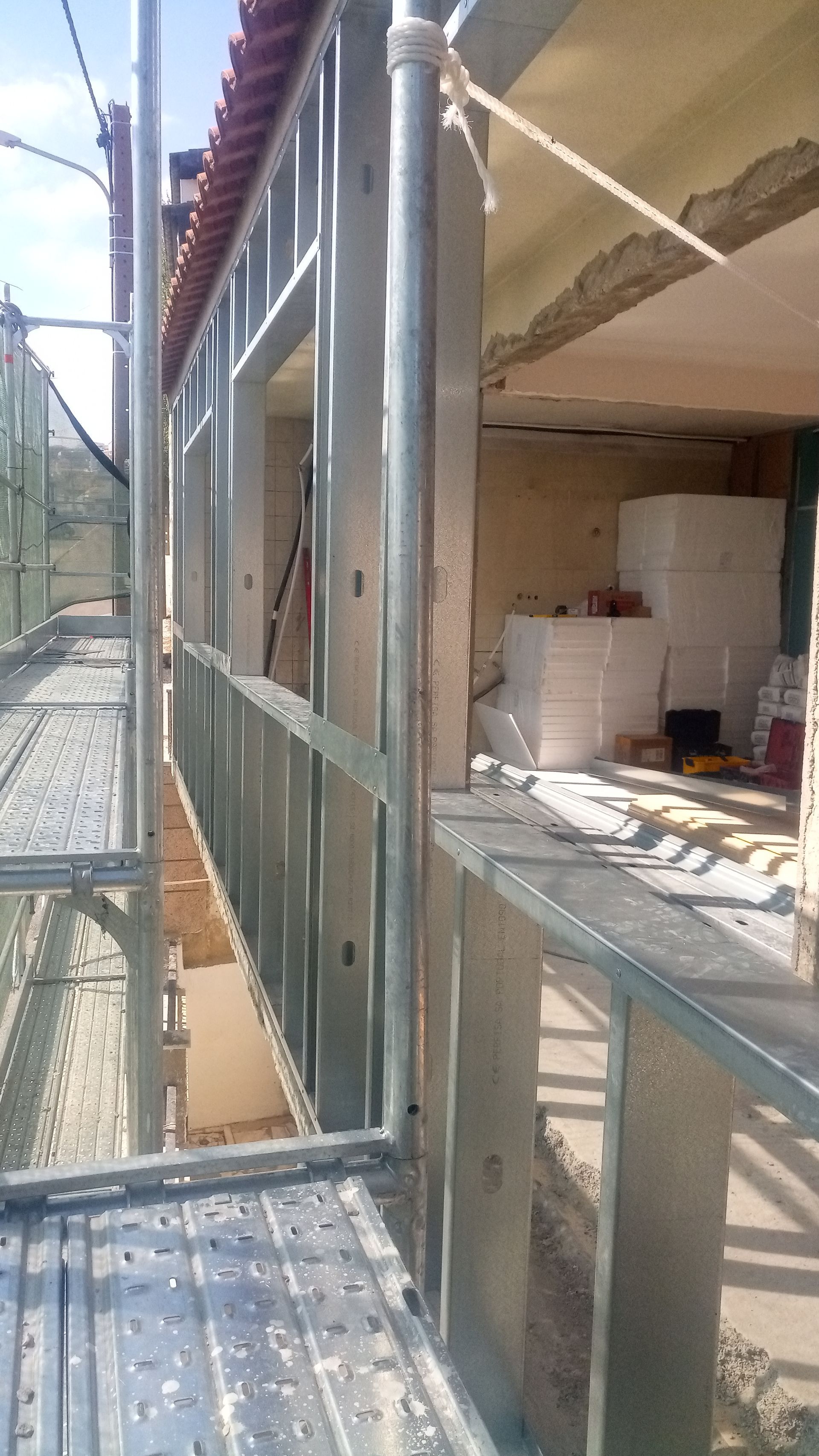Andaimes ao lado de um prédio em construção; estrutura metálica visível, janela aberta.