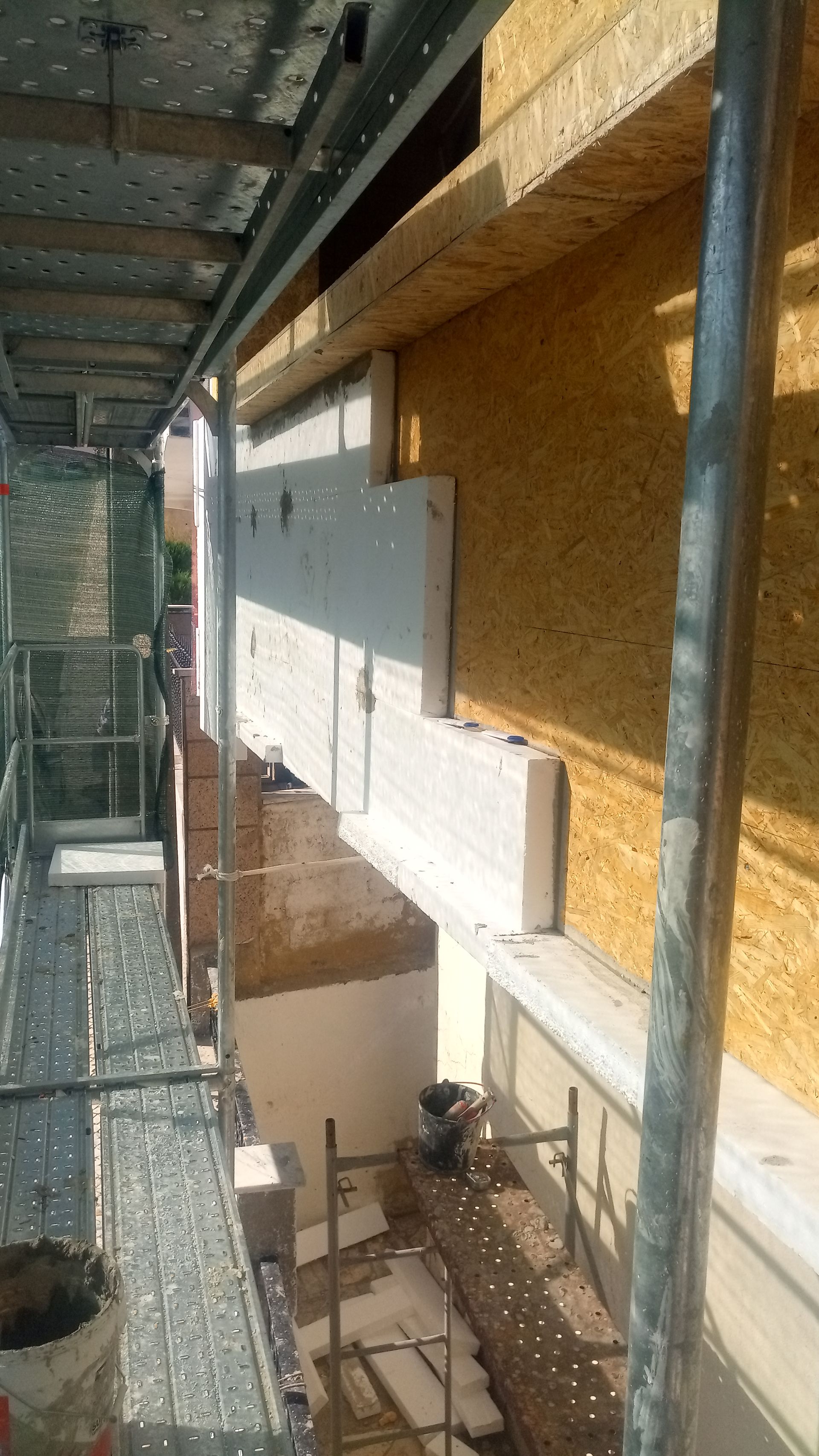 Canteiro de obras: viga de concreto cinza instalada em um edifício com revestimento de madeira, vista de um andaime.