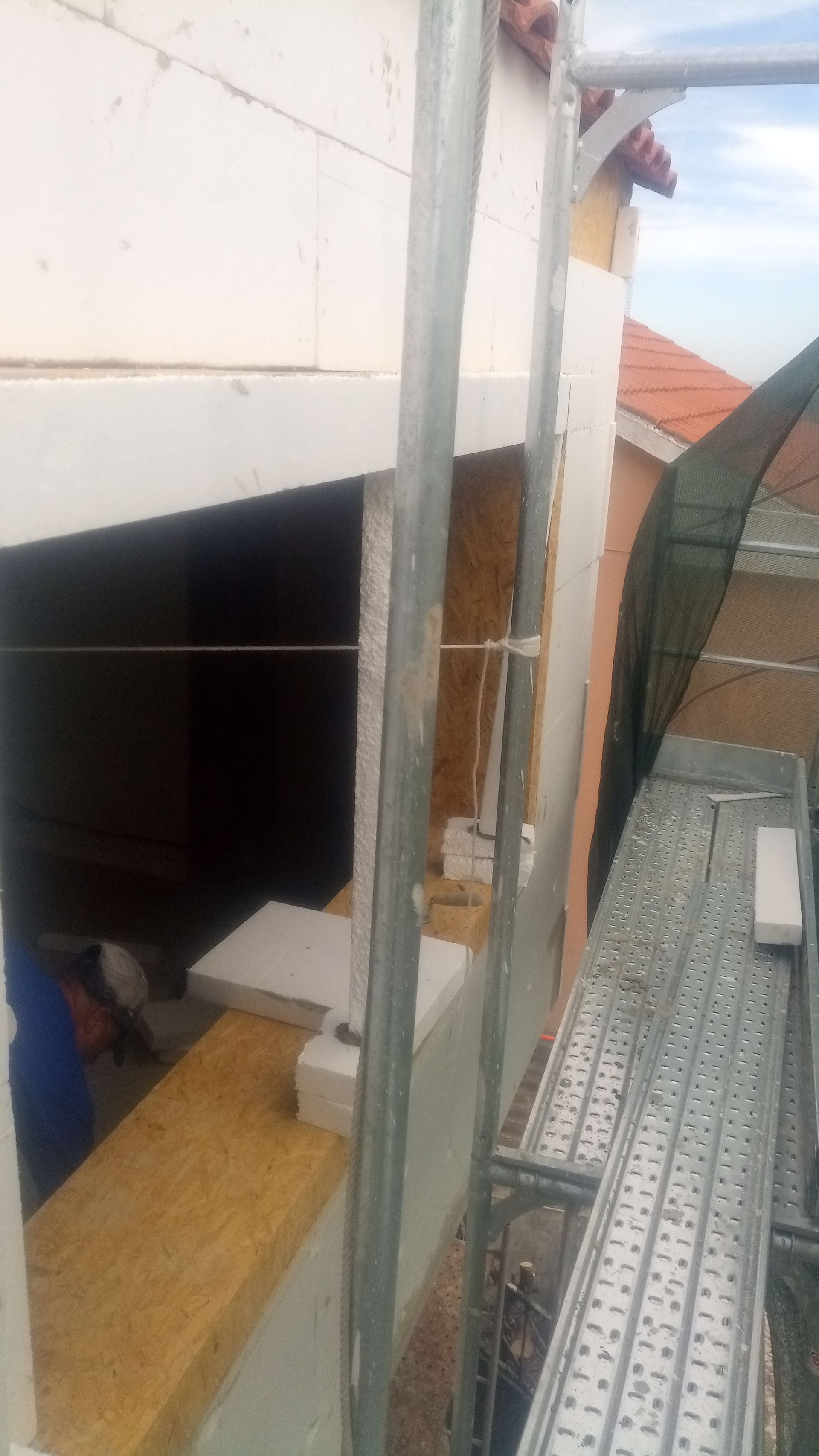 Operário da construção civil trabalhando na parte externa de um prédio, utilizando escada e andaime.