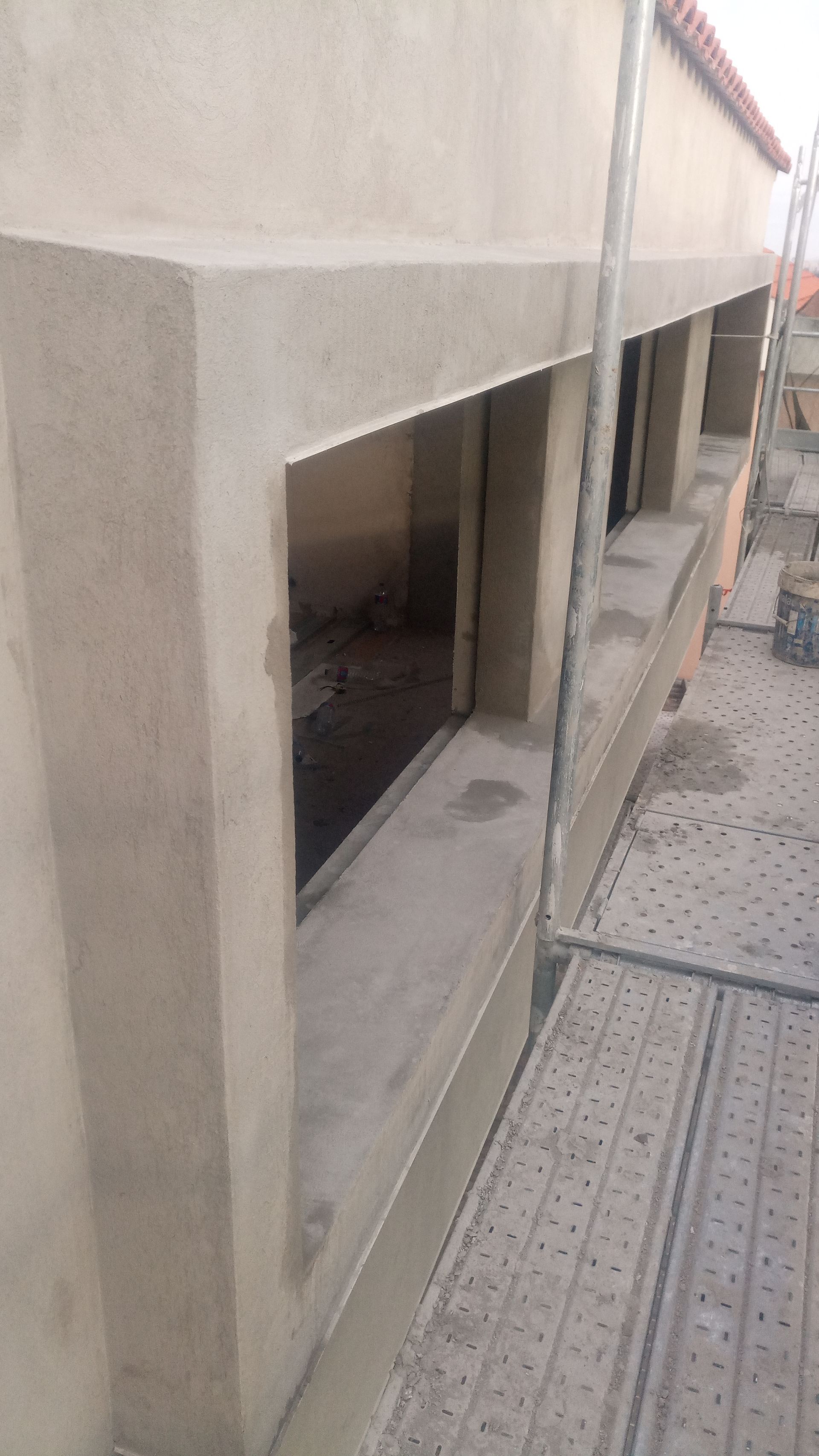 Exterior de um edifício em construção, mostrando uma moldura de janela e andaimes. Estuque cinza e concreto.