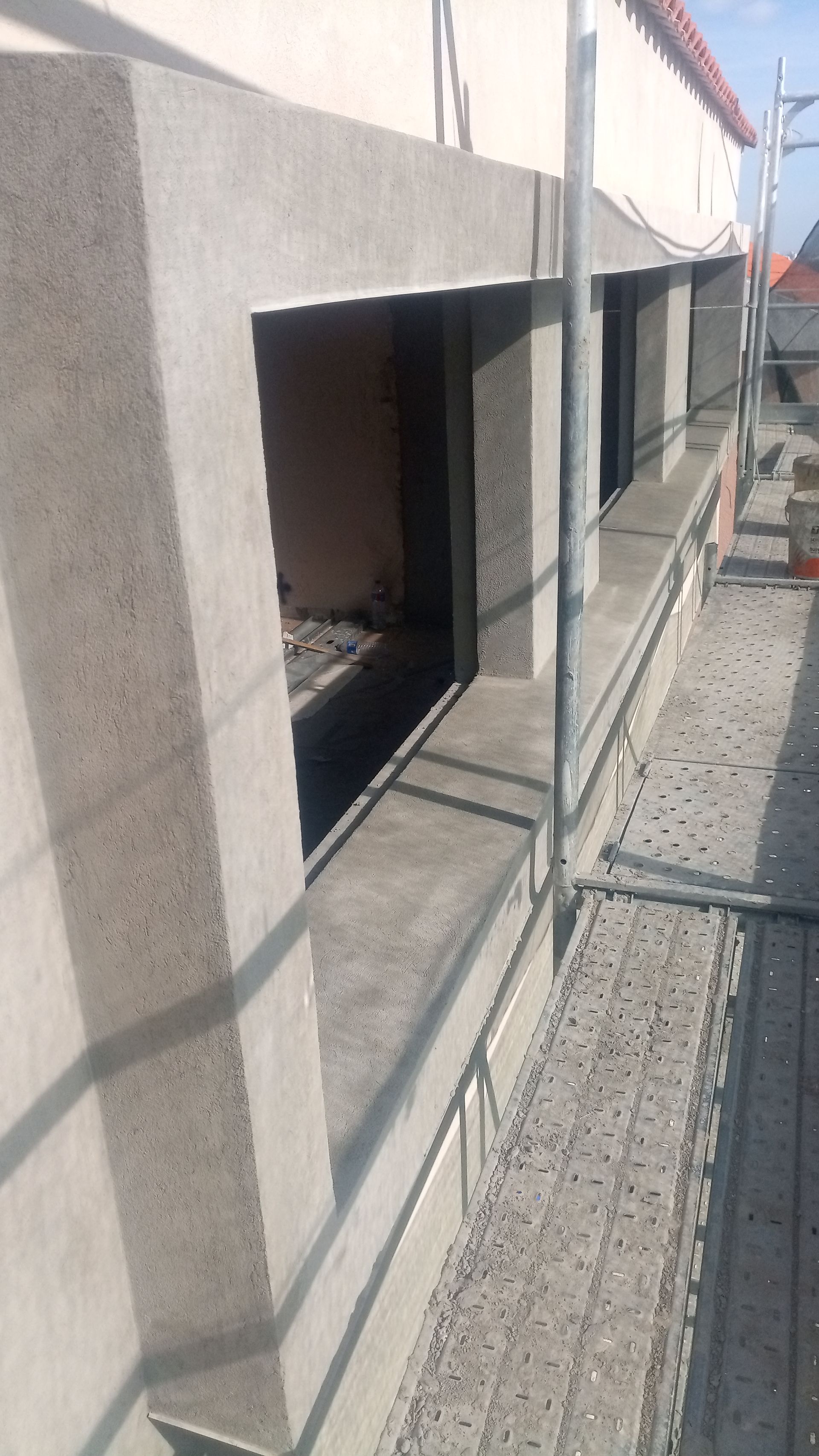 Caixilhos das janelas exteriores, recém-rebocados, em construção com andaimes. Tons de cinza, muita luz natural.