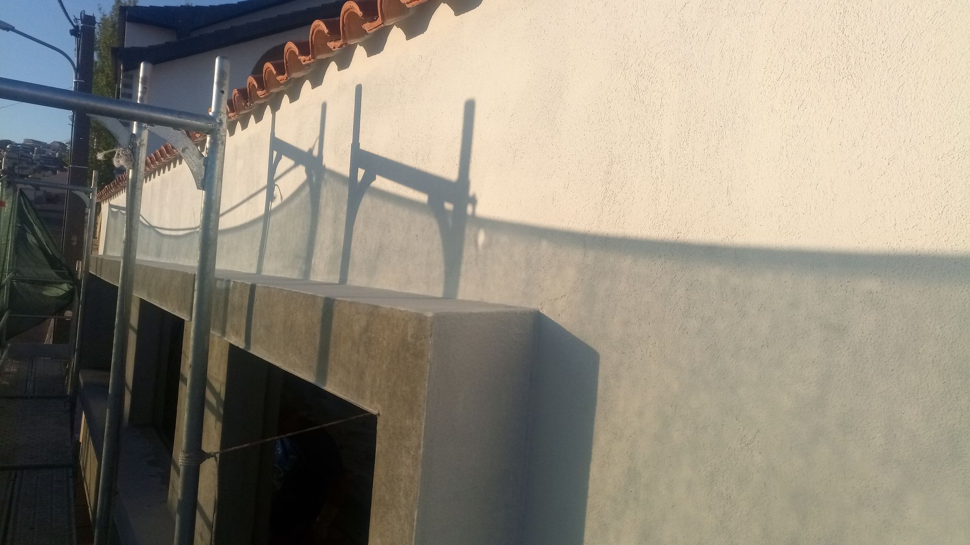 Fachada cinza do prédio com parede curva, telhado de telha vermelha e grade de metal.