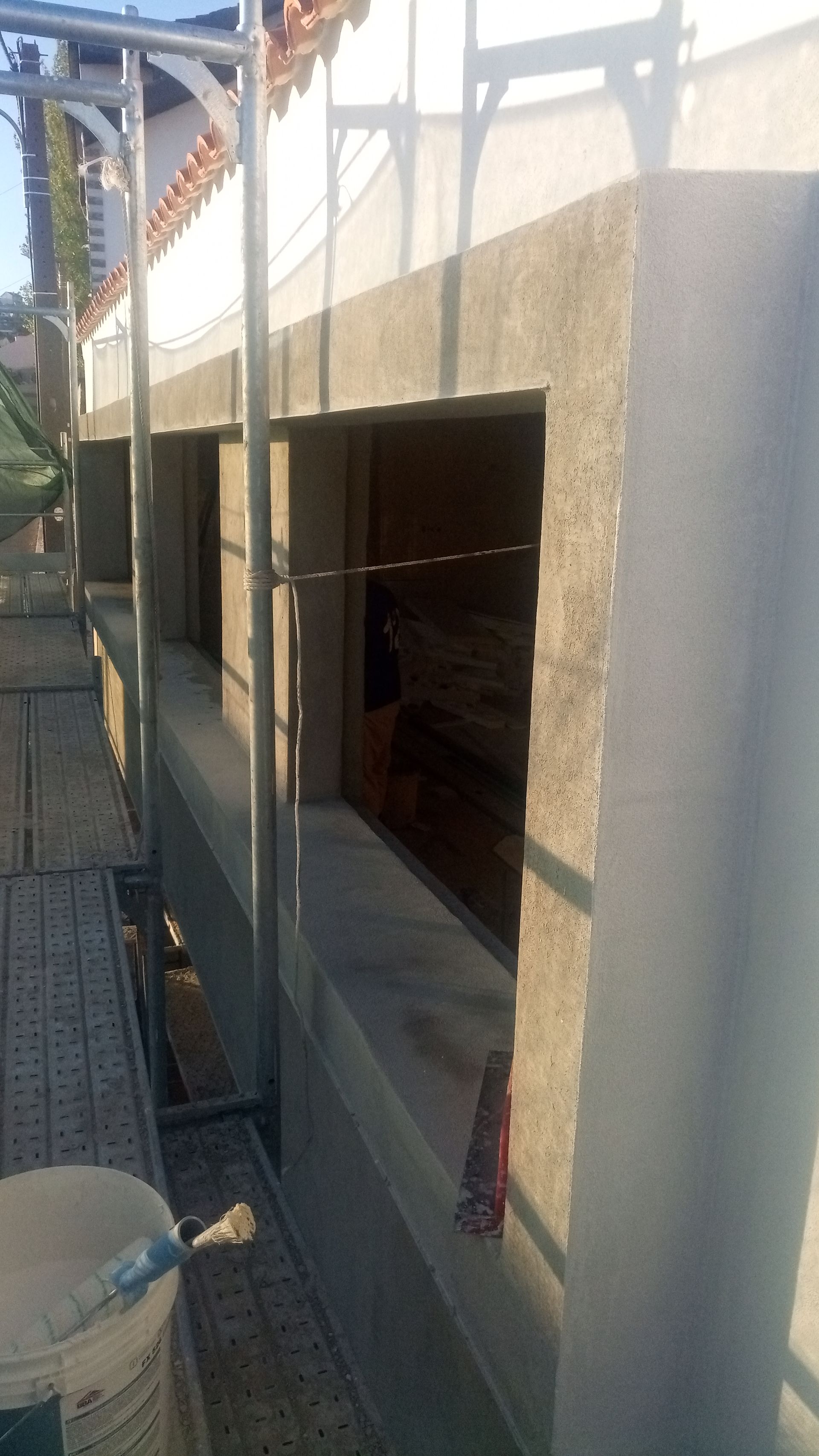 Canteiro de obras com parede de concreto inacabada e aberturas para janelas, com andaimes ao lado.