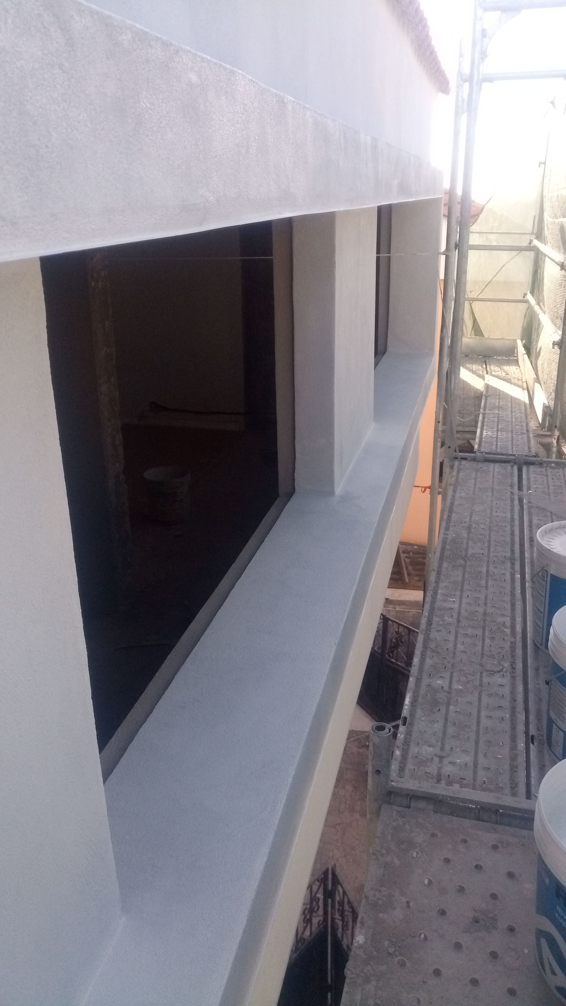 Exterior de um edifício com janelas recém-rebocadas, andaimes e baldes de tinta.