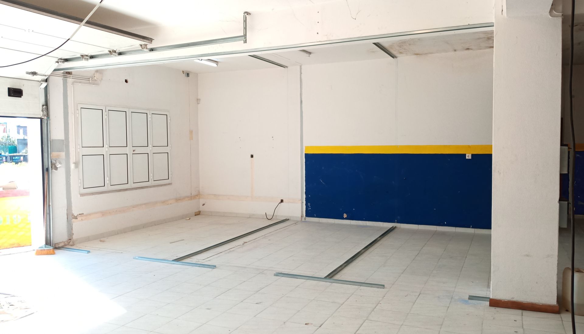 Espaço comercial vazio com paredes brancas, detalhes em azul e amarelo e piso de azulejo.