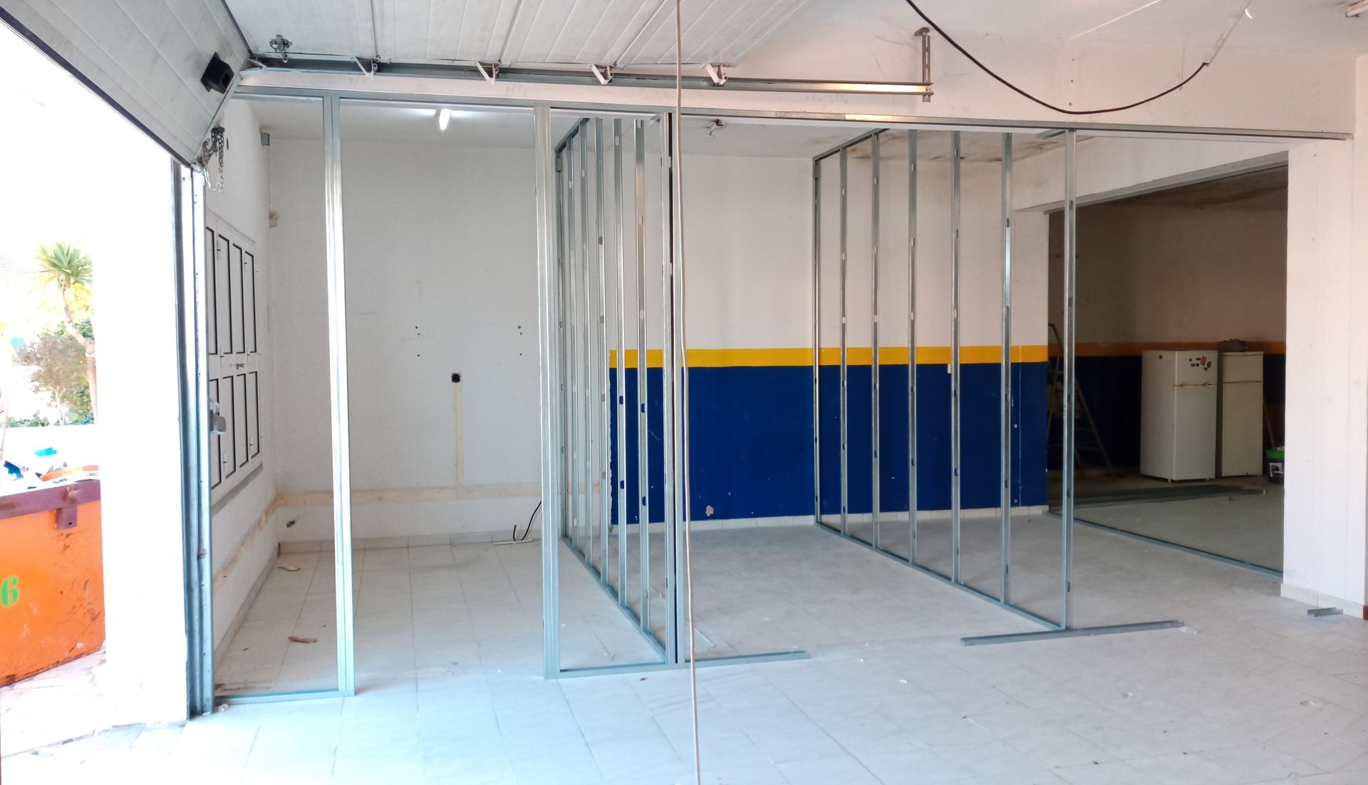 Espaço interior com estrutura de metal para novas paredes, paredes pintadas de branco e azul, iluminação fluorescente.