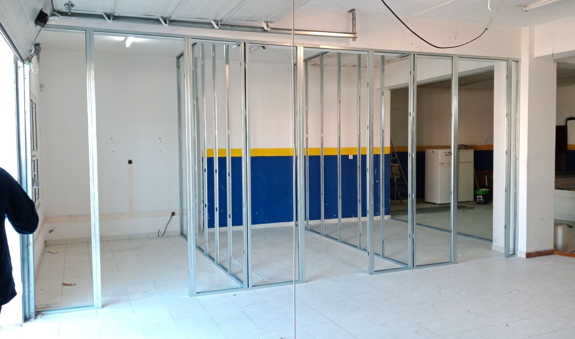 Perfis metálicos delimitando as paredes de um cômodo em construção; paredes pintadas de branco, azul e amarelo.