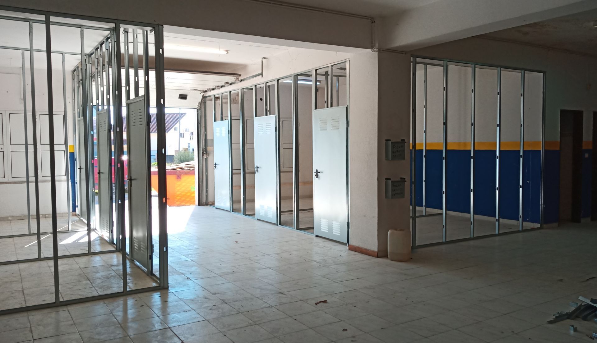 Interior em construção com estrutura metálica, portas e parte da parede em tons de azul e amarelo.