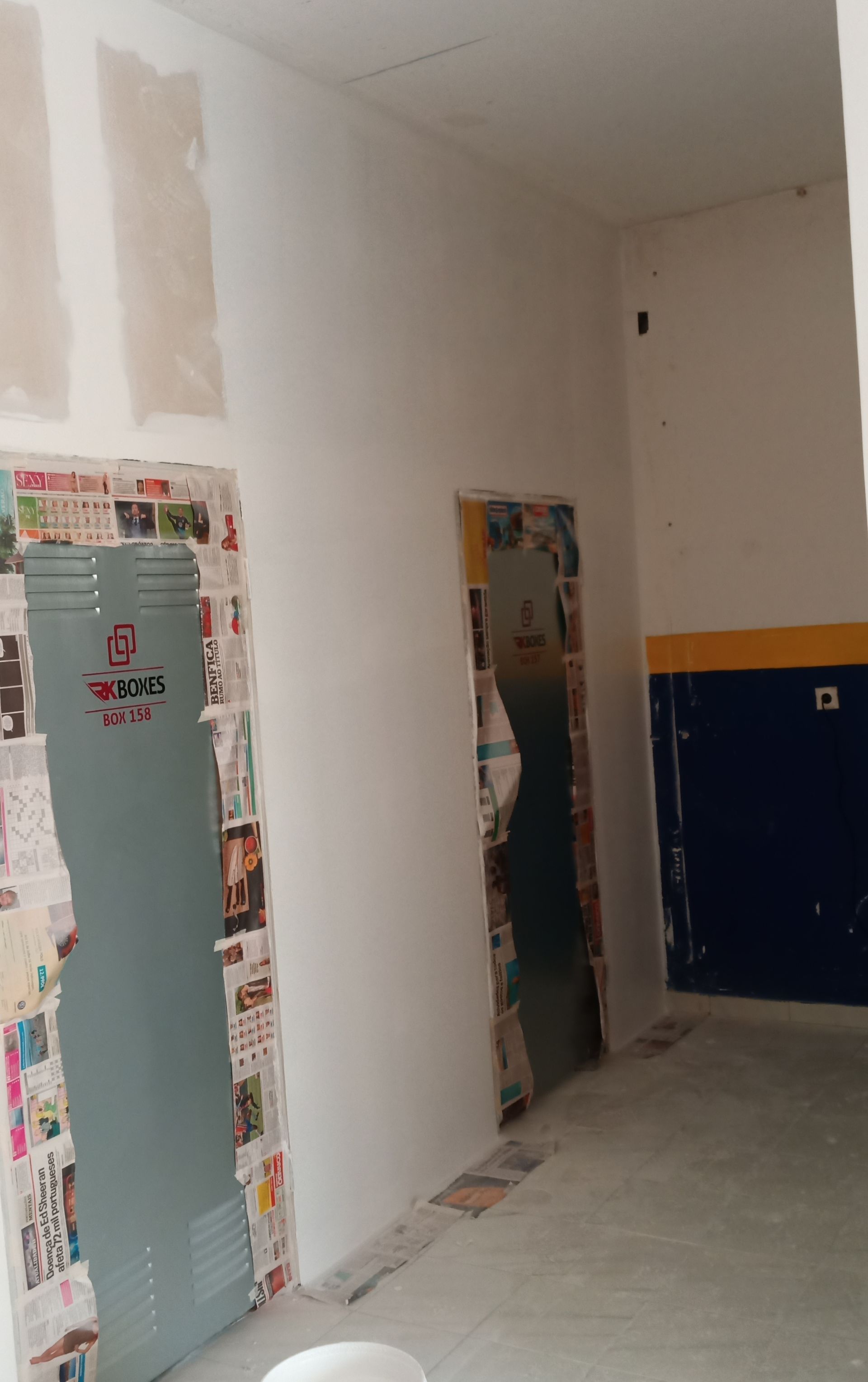 Corredor com paredes inacabadas, portas cobertas com jornal e uma parede parcialmente pintada.