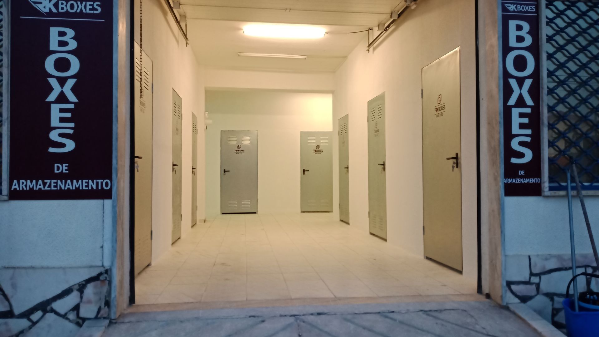 Entrada de um depósito com uma fileira de portas cinzentas fechadas e uma placa que diz 