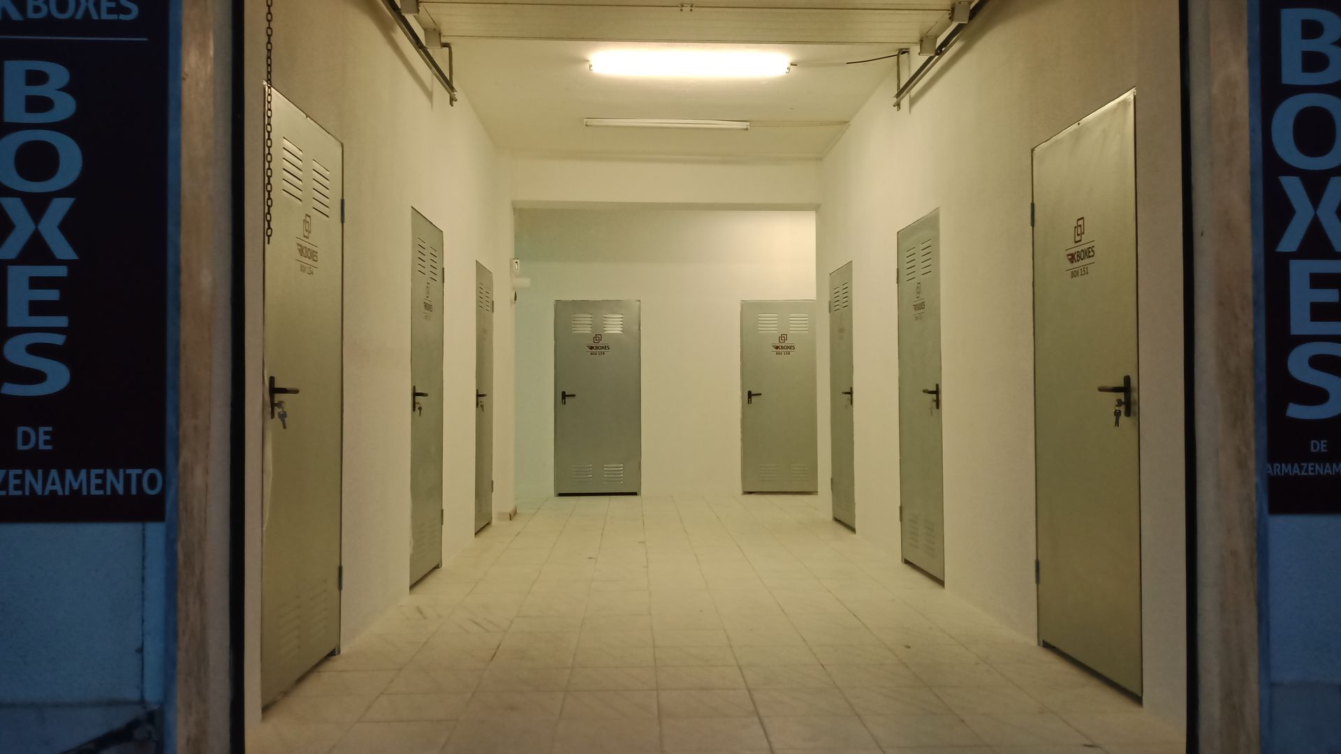Corredor com armários de armazenamento cinza, iluminação no teto e paredes brancas.