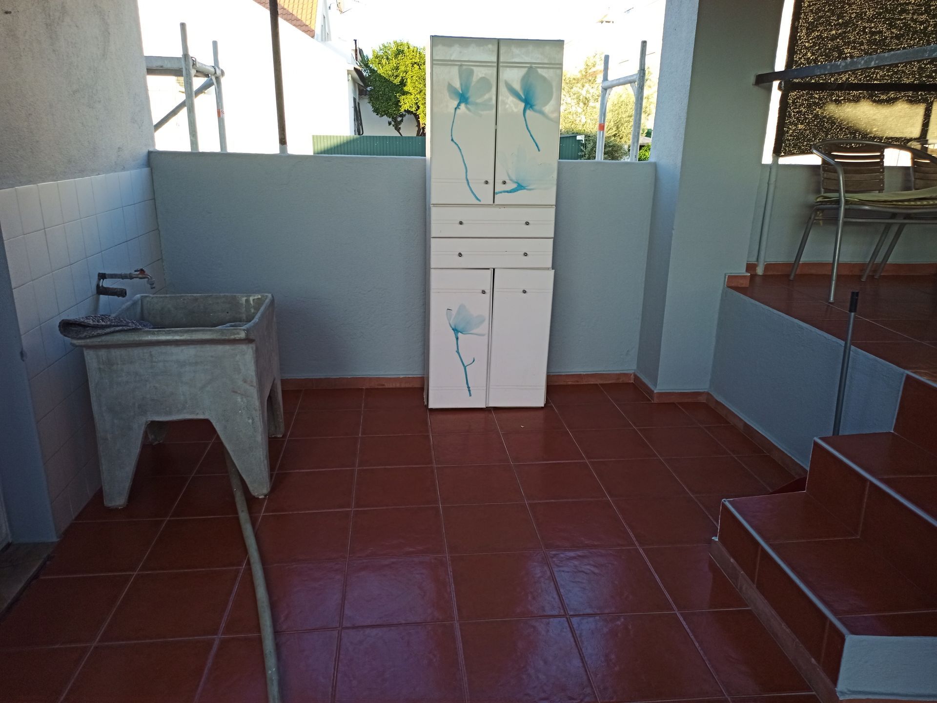 Lavanderia com armário e pia; piso de azulejo vermelho, paredes cinza.