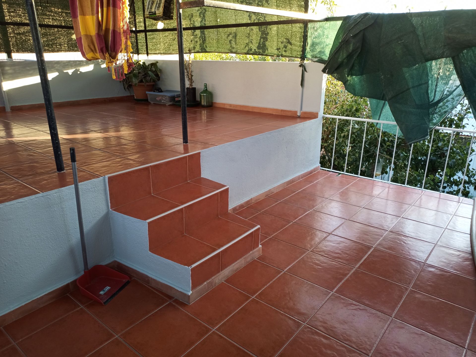 Terraço com piso e degraus de ladrilho laranja. Paredes brancas, uma rede e um parapeito com vista para as árvores.