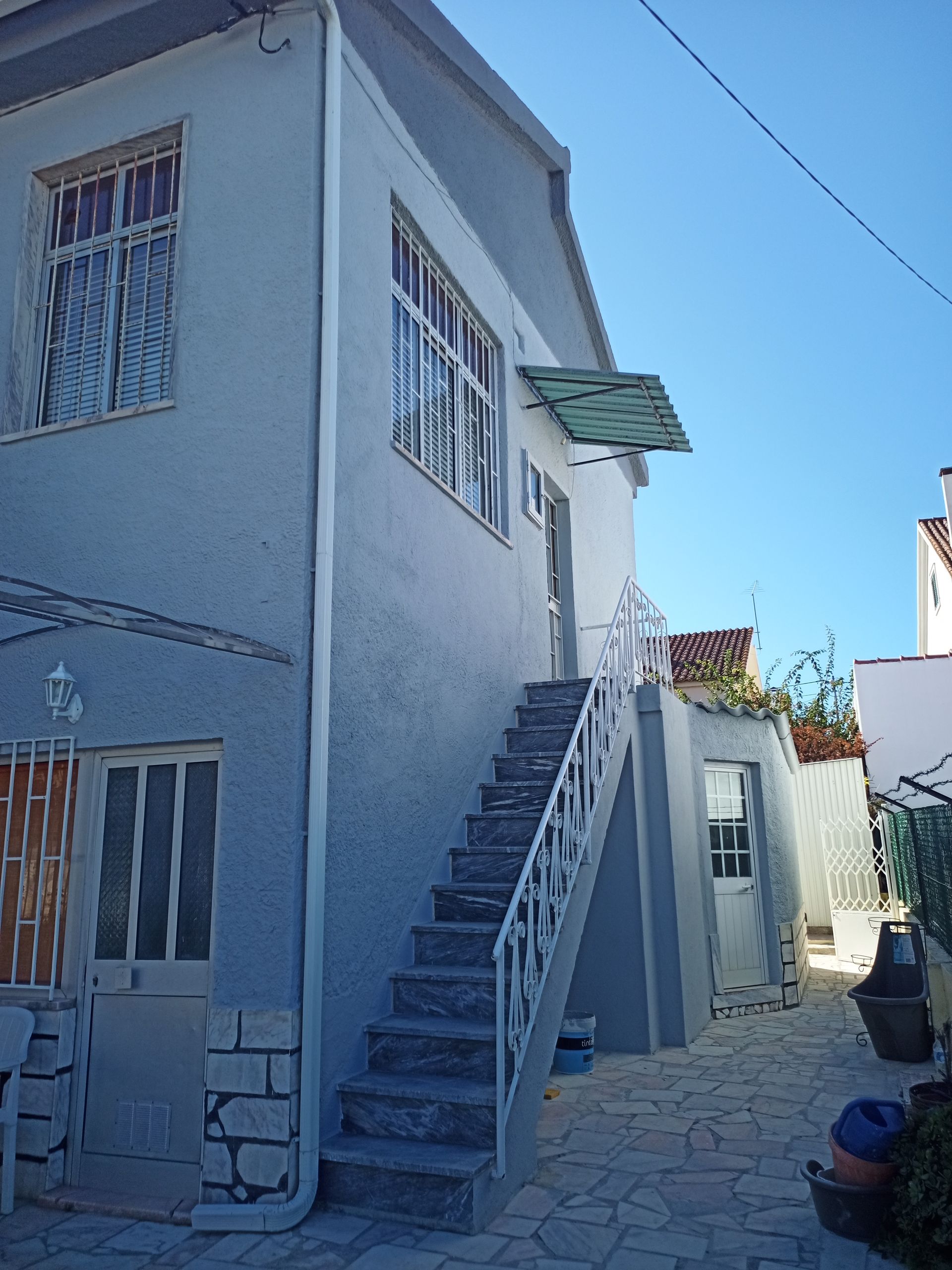 Prédio azul claro de dois andares com escada externa e pequeno toldo sobre a porta.
