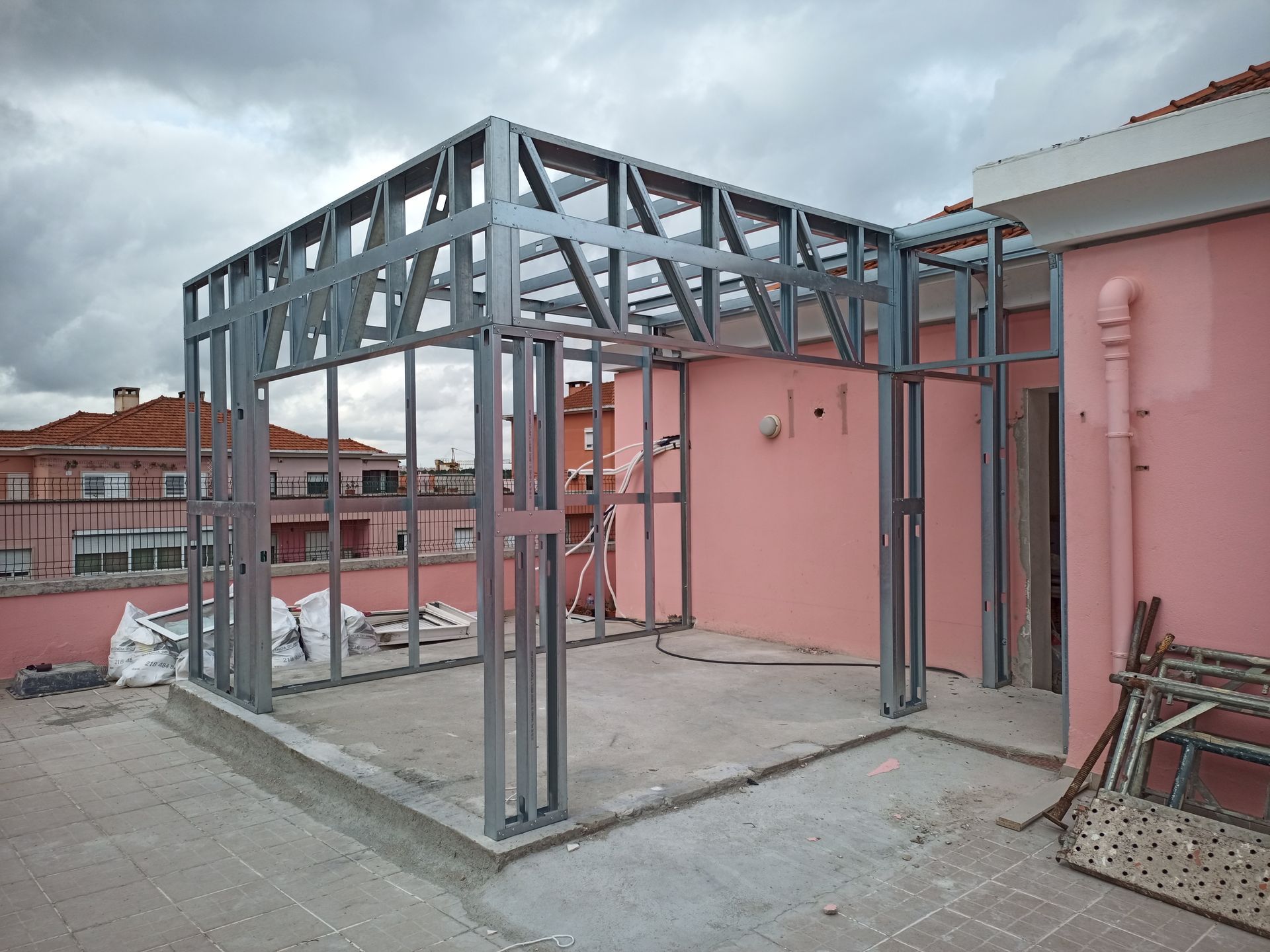 Estrutura metálica sendo construída em um telhado, com um prédio rosa ao fundo.