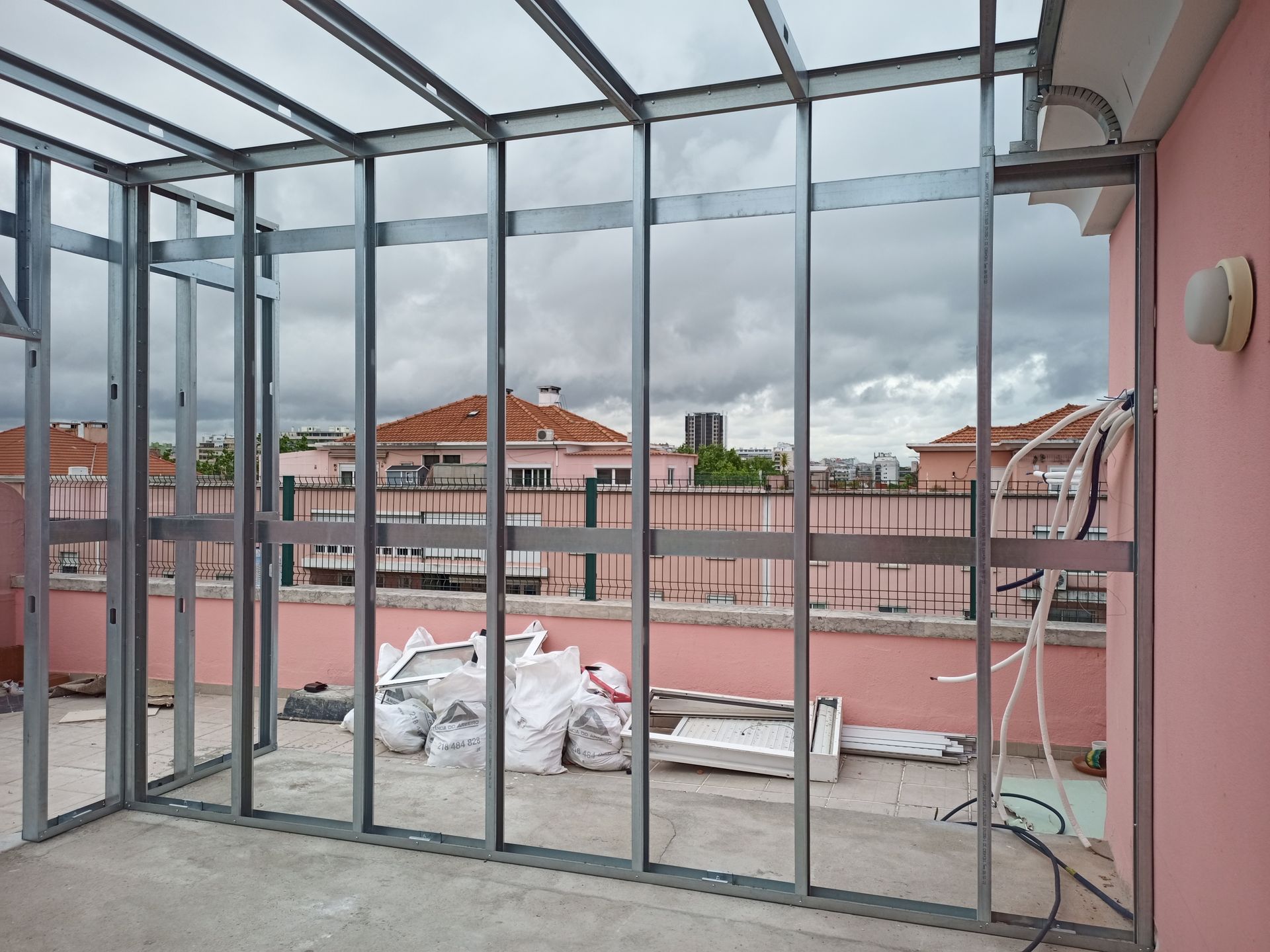 Estrutura metálica para a construção de uma varanda envidraçada em um terraço, com céu nublado ao fundo.