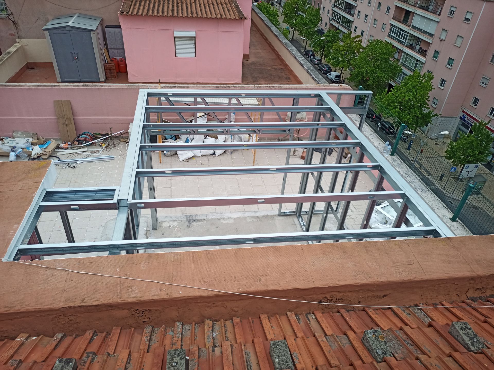 Estrutura metálica sobre um telhado, com edifícios circundantes e alvenaria visíveis.