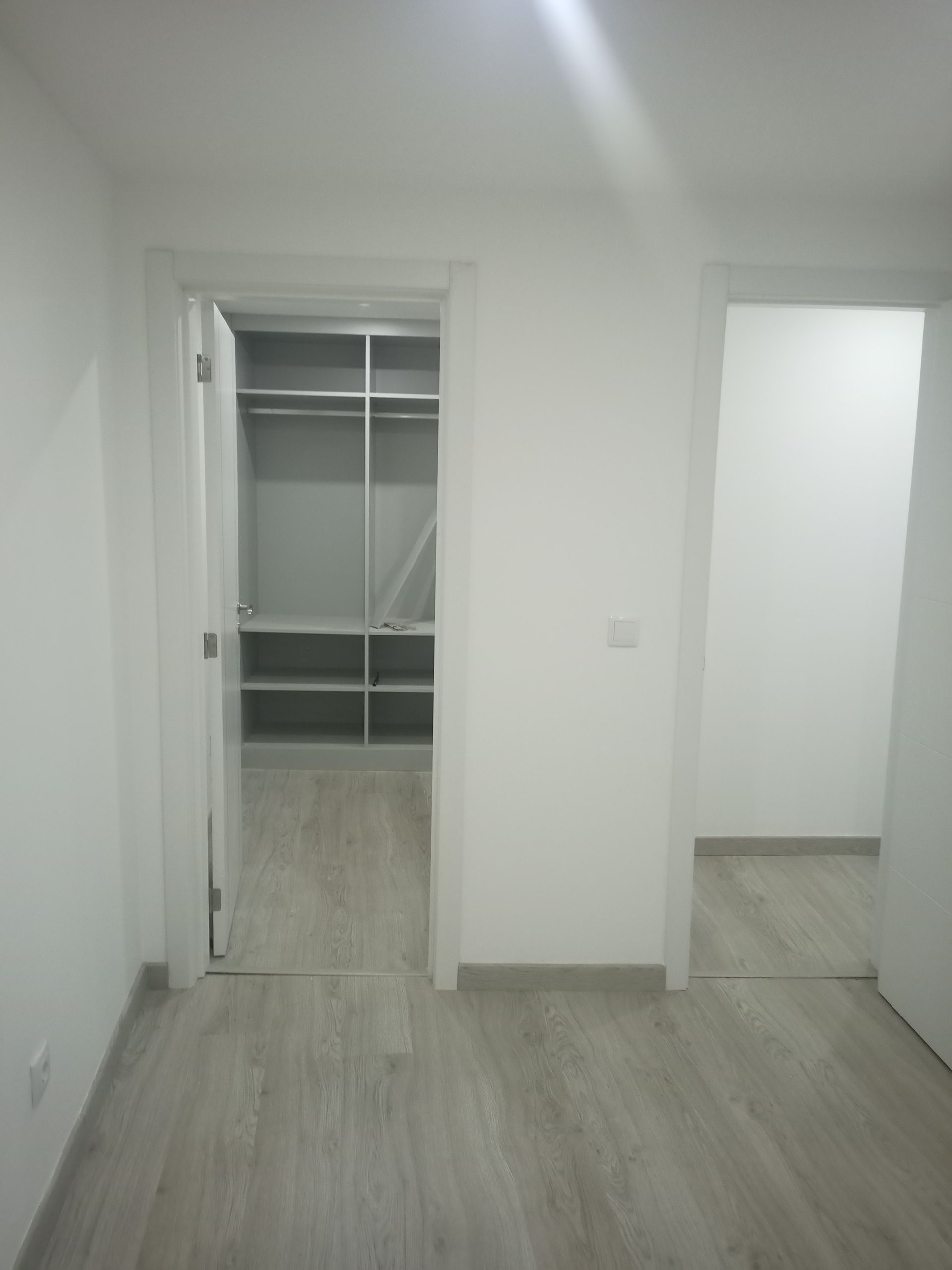 Quarto com piso de madeira cinza claro, duas portas que dão acesso a um closet e a outro cômodo.