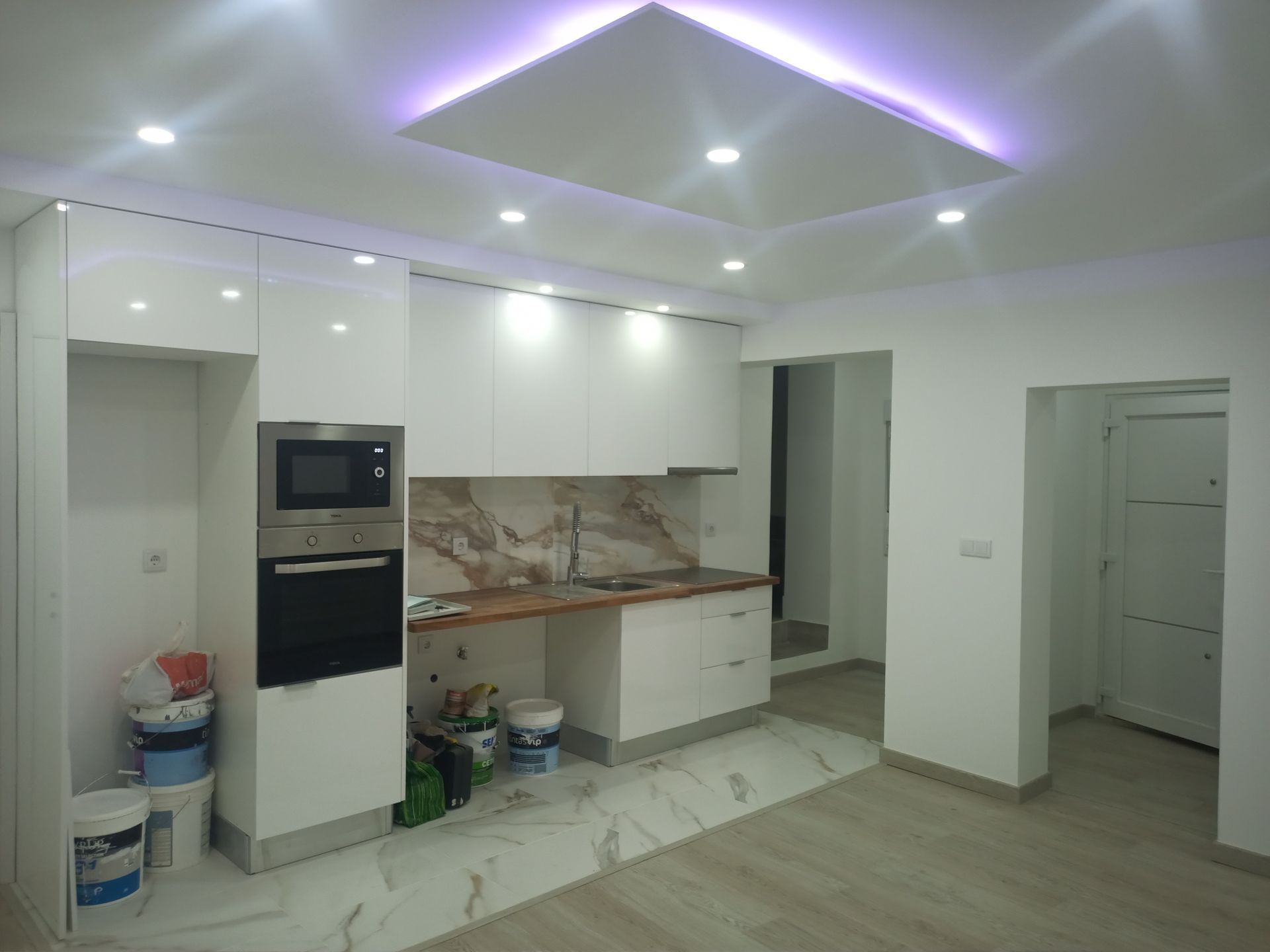 Cozinha moderna com armários brancos, forno embutido, backsplash de mármore e iluminação embutida.
