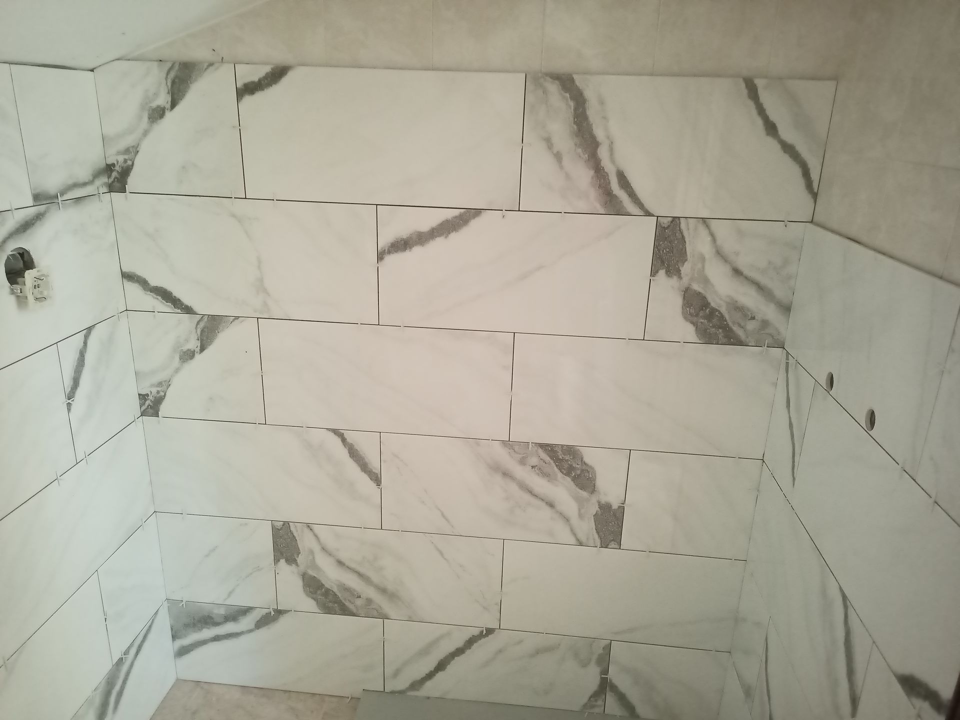 Azulejos marmorizados brancos e cinza instalados na parede do chuveiro.