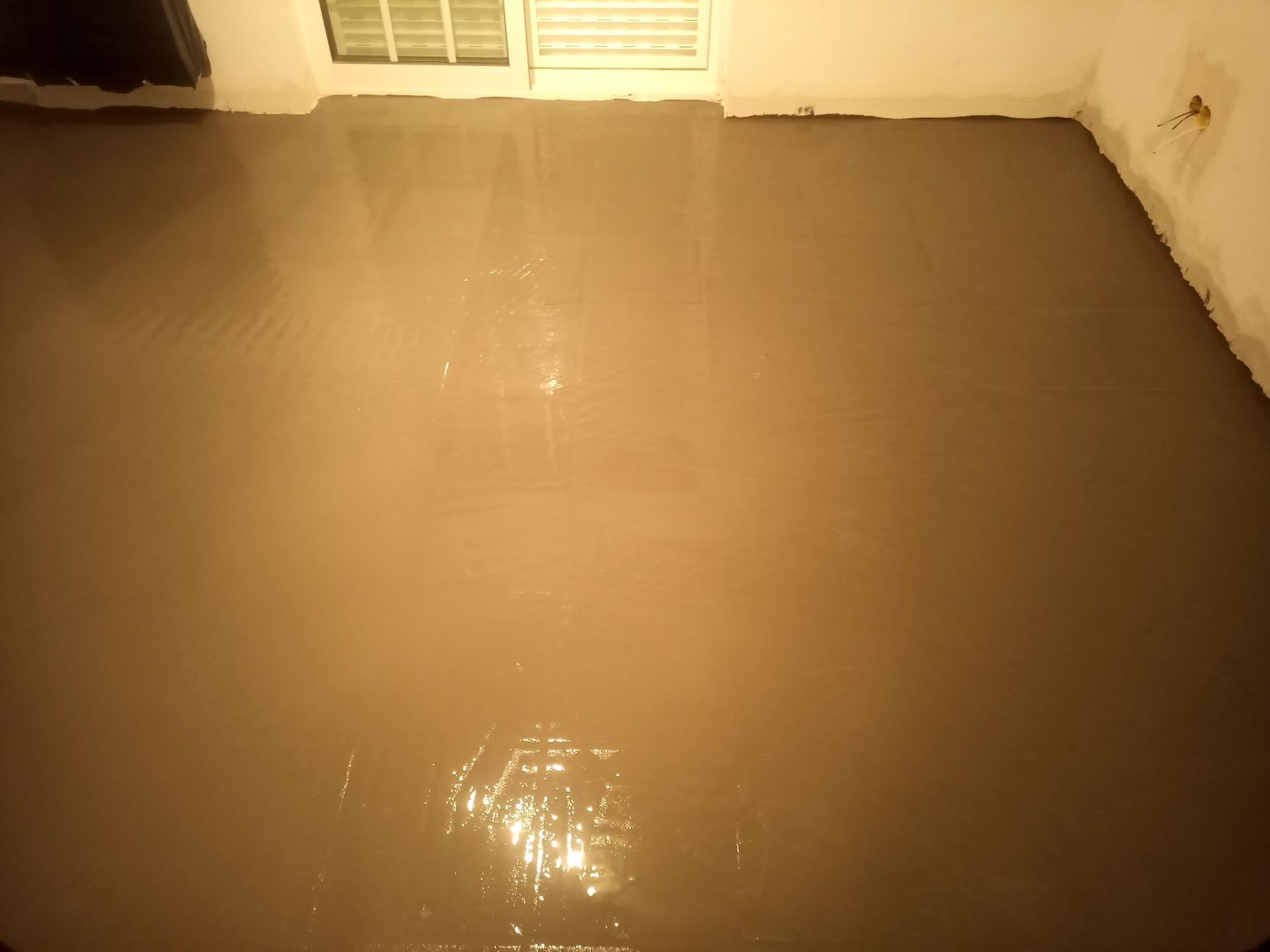 Piso de concreto recém-despejado, úmido e nivelado em um cômodo.