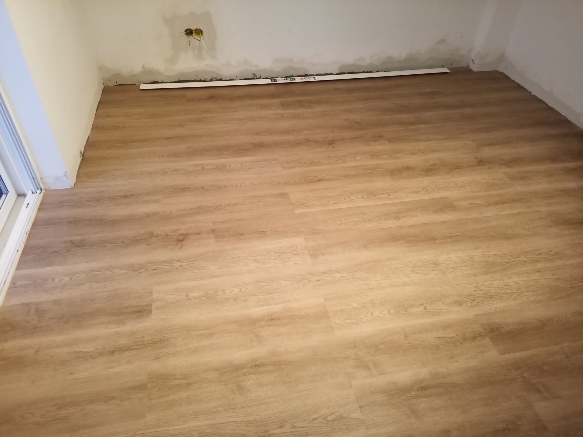 Quarto com piso novo imitando madeira em tom castanho claro; rodapés parcialmente instalados junto à parede.