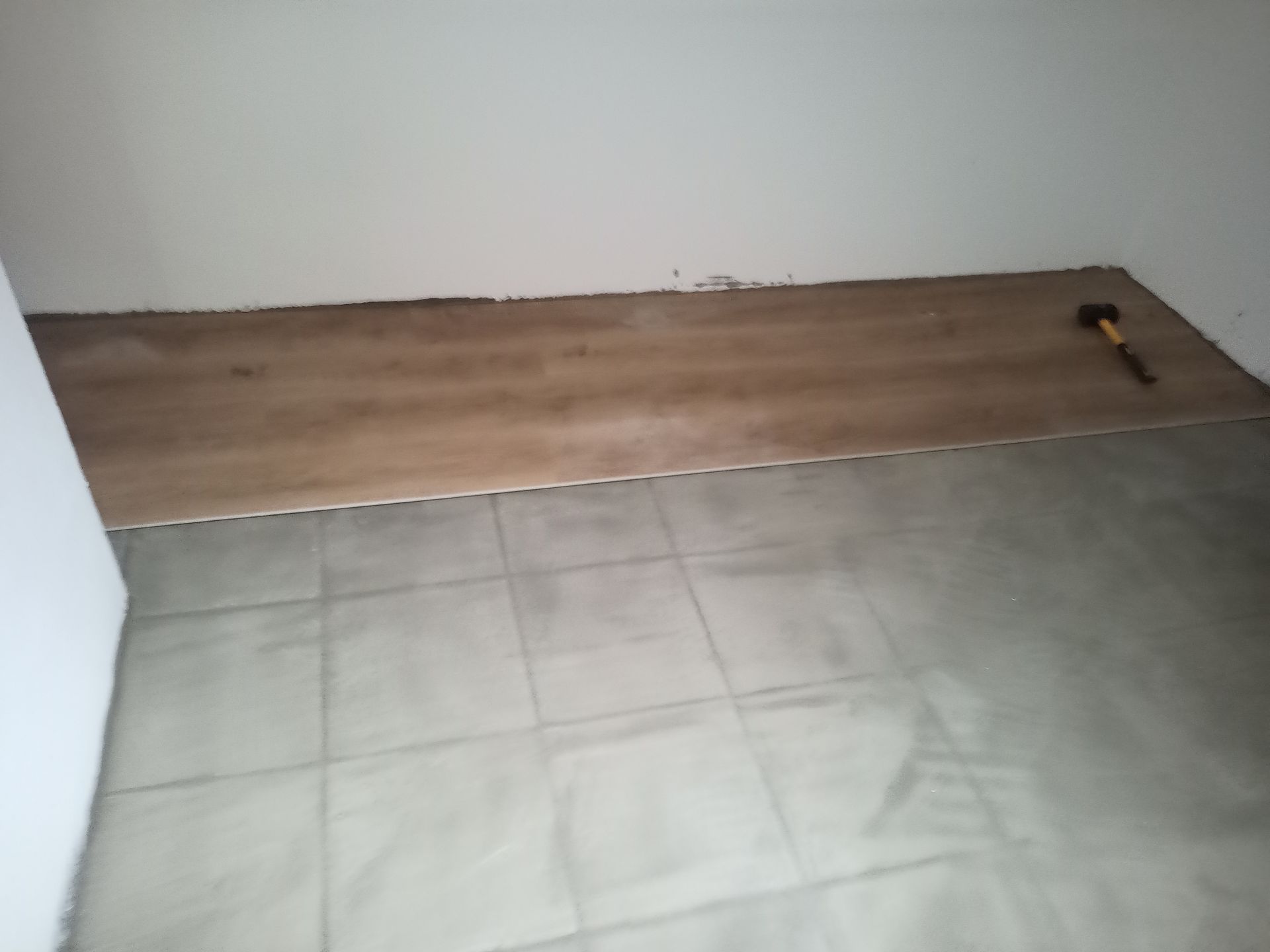 Piso de madeira sendo instalado sobre piso de cerâmica. Martelo apoiado no piso novo.
