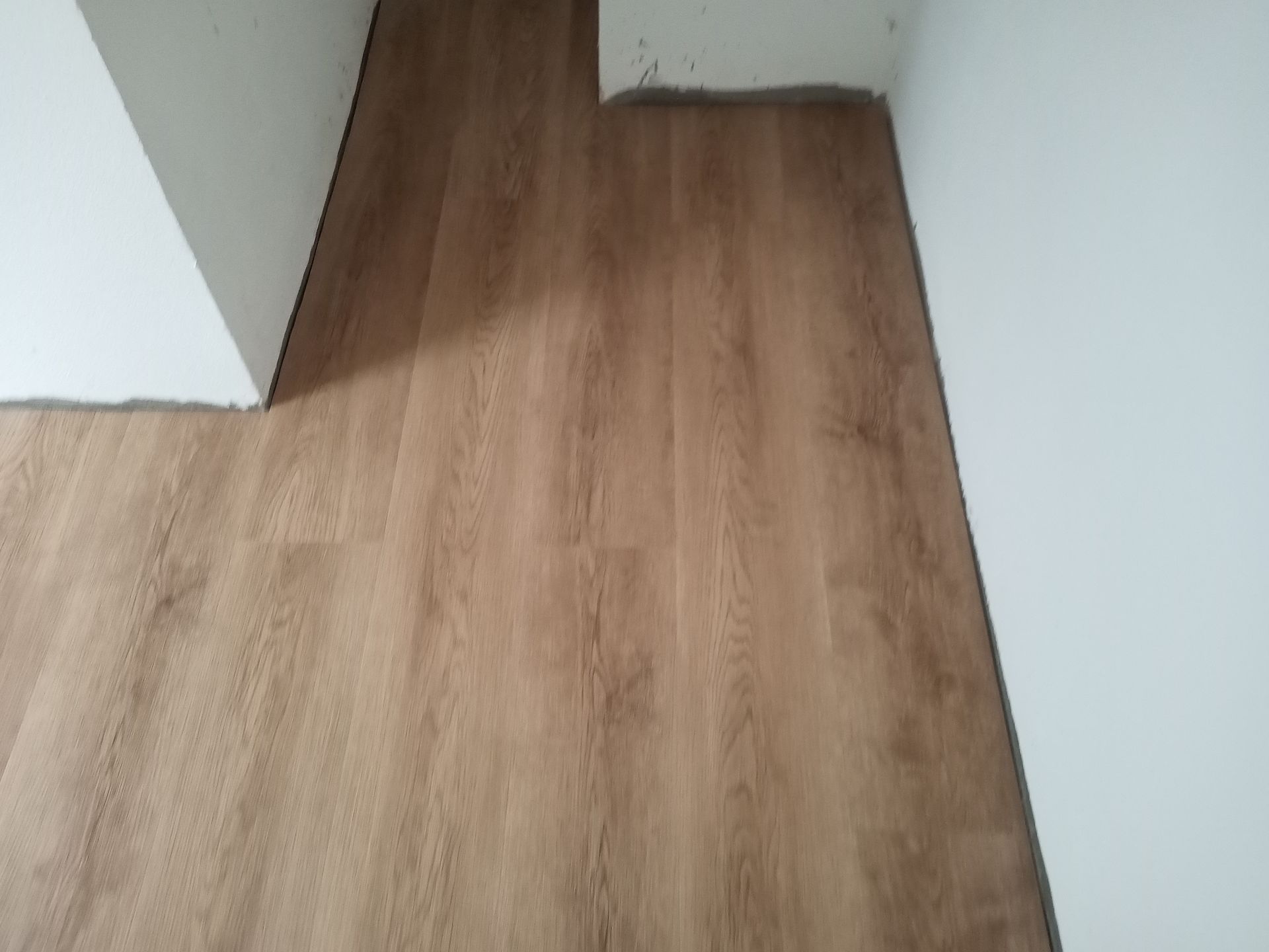Piso com aparência de madeira instalado contra paredes brancas em um cômodo, com o piso visível em toda a imagem.