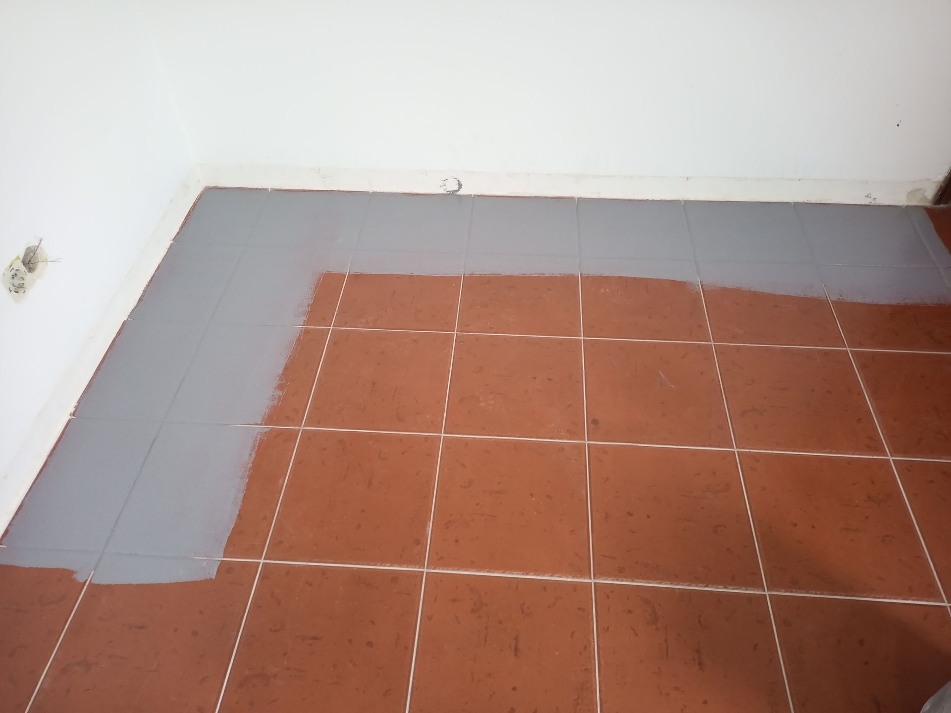 Tinta cinza aplicada no piso de ladrilhos de terracota em um canto da sala, cobrindo parcialmente os ladrilhos.
