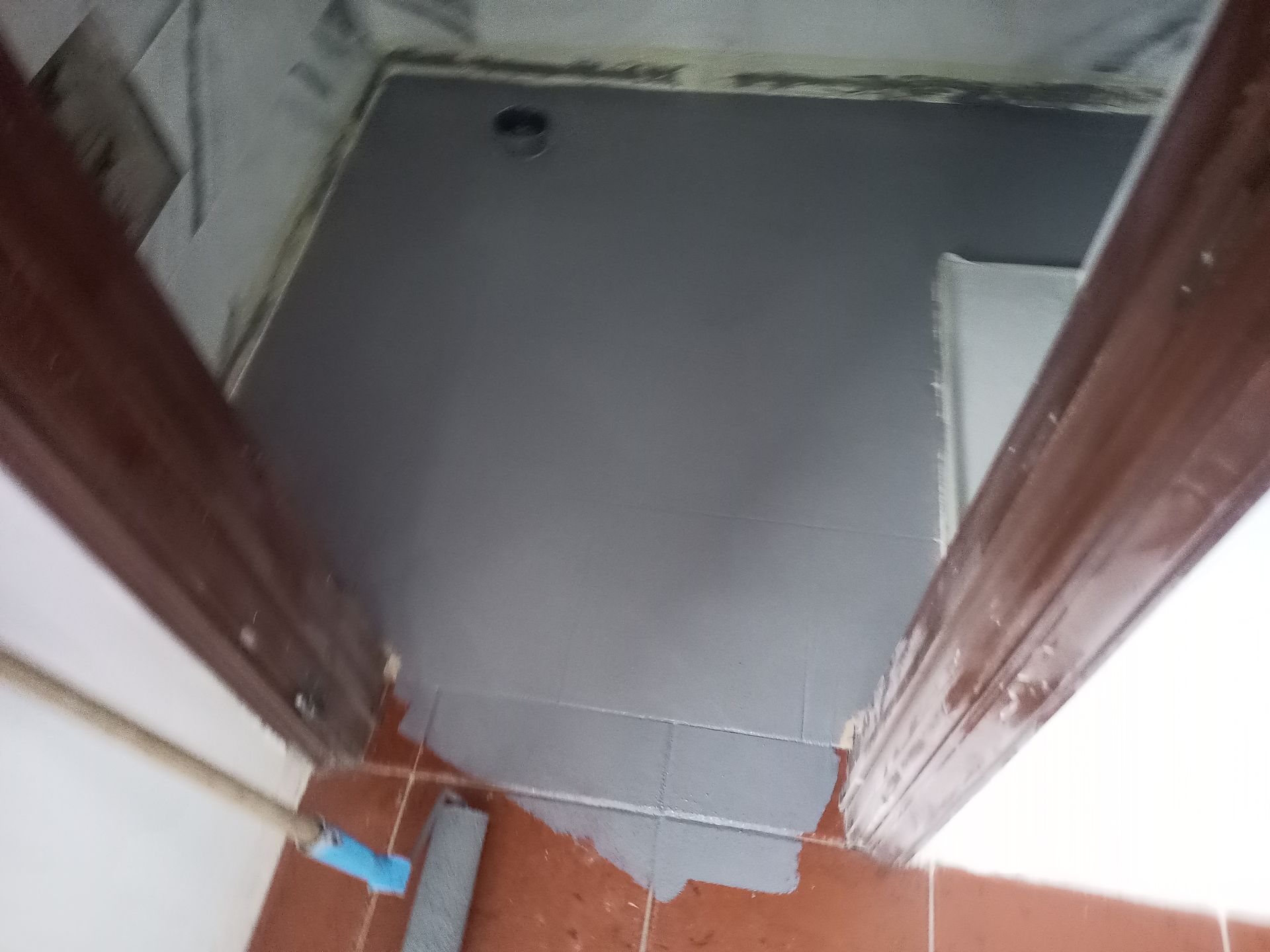 Piso do banheiro sendo pintado de cinza, visto da porta.