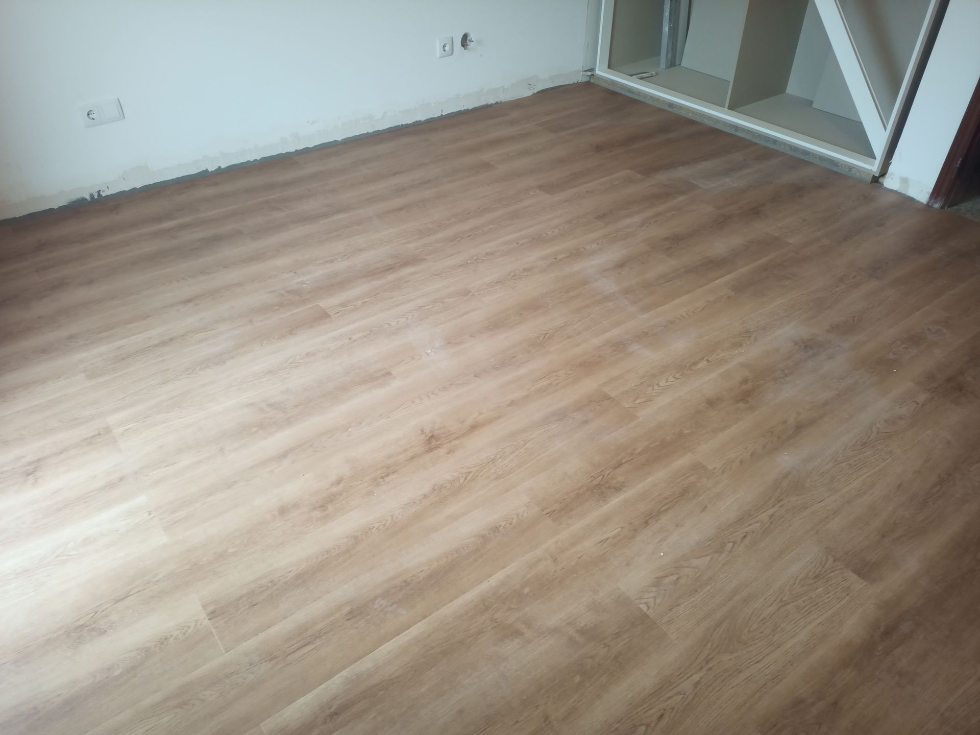 Piso laminado imitando madeira recém-instalado em um cômodo. Cor marrom claro, com um armário parcialmente embutido.
