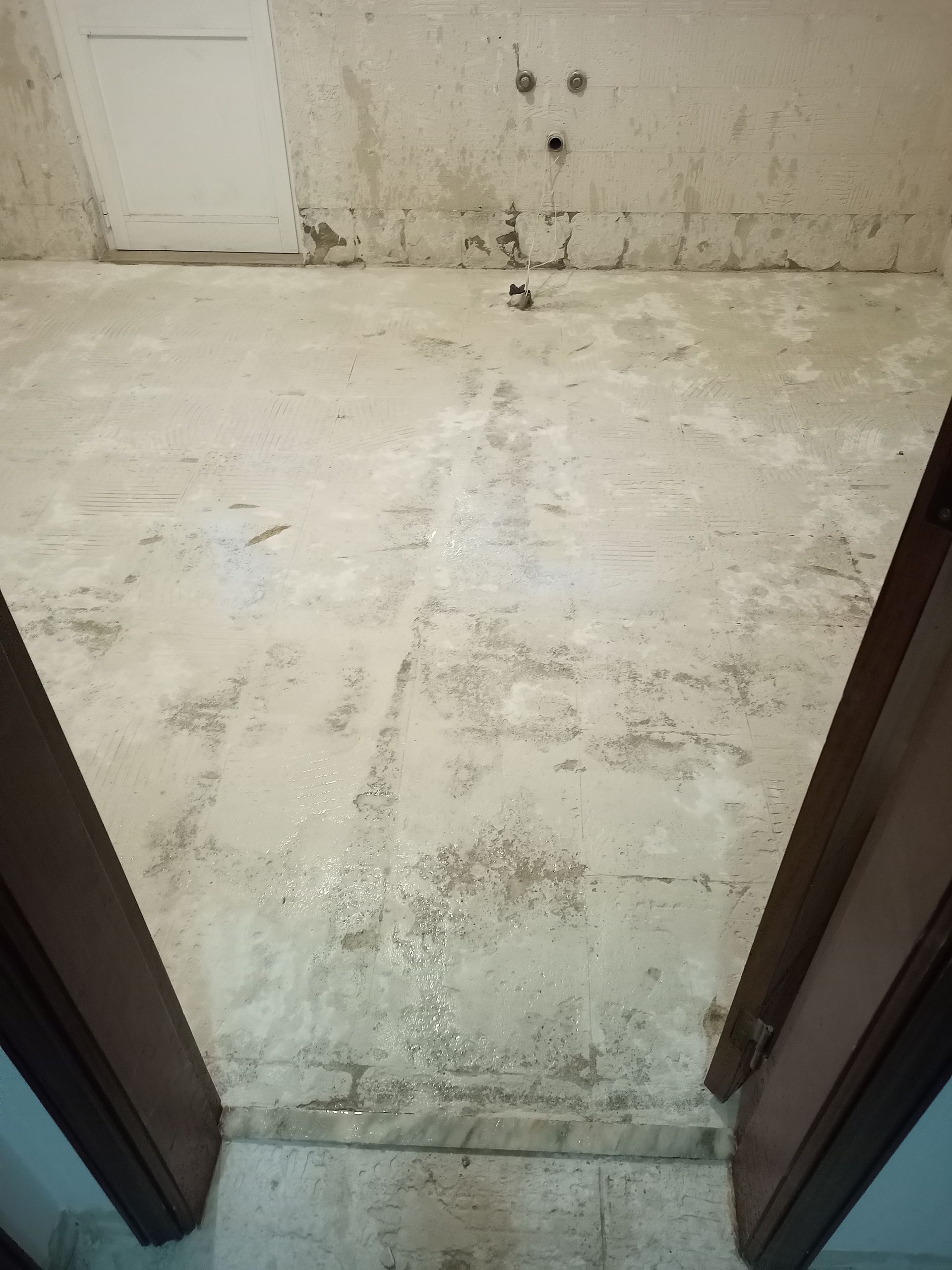 Sala de cimento aparente com manchas nas paredes e no chão, vista da porta.