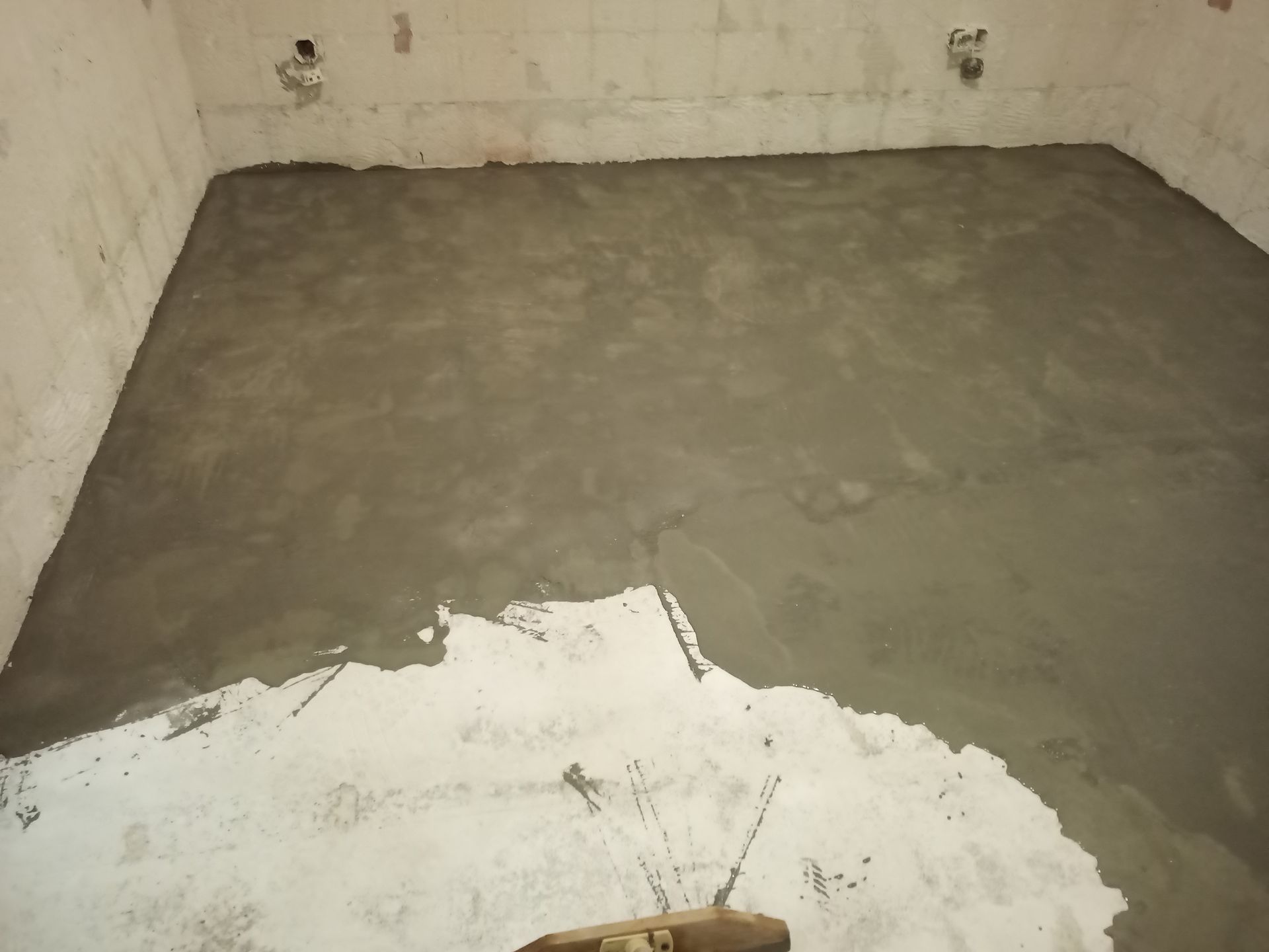 Piso de concreto cinza liso e recém-moldado em uma sala com paredes brancas, em construção inacabada.
