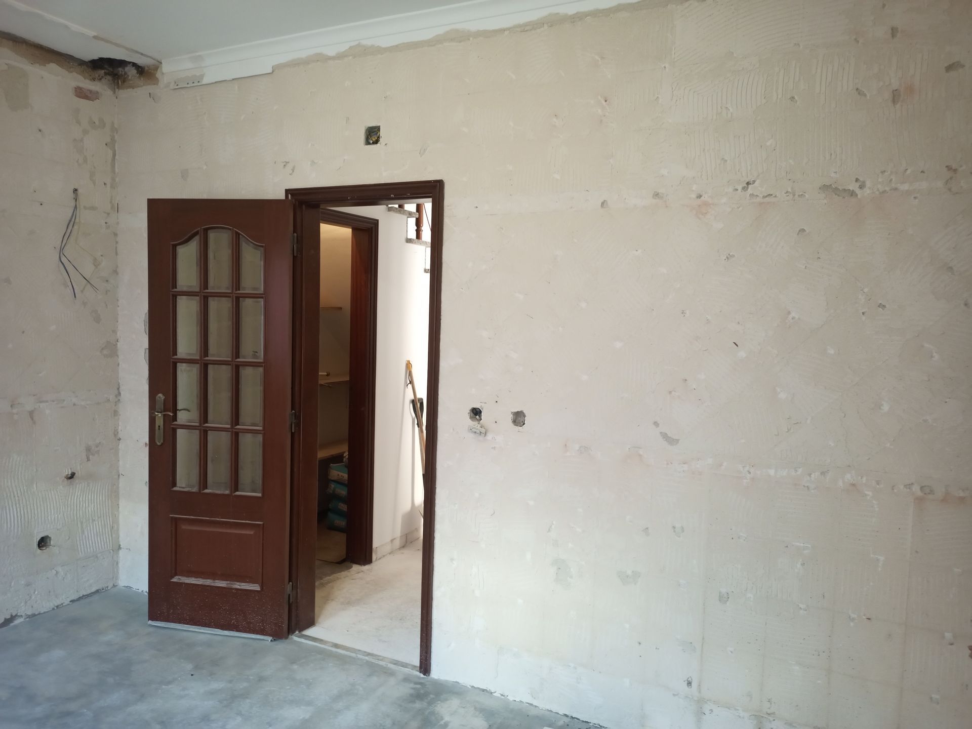 Quarto interior com portas de madeira abertas, paredes nuas e uma vista parcial para outro cômodo.