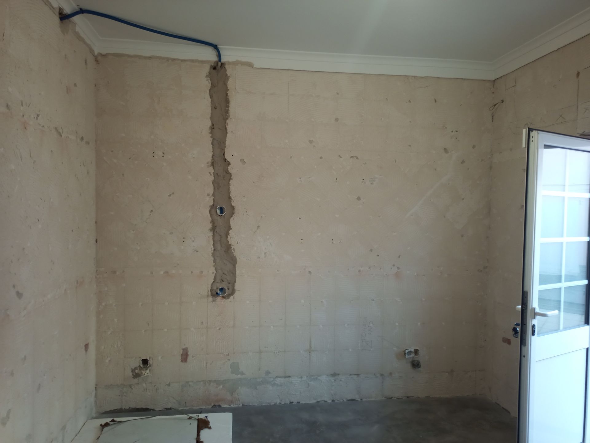 Parede interna com fiação exposta, textura inacabada e porta parcialmente aberta.