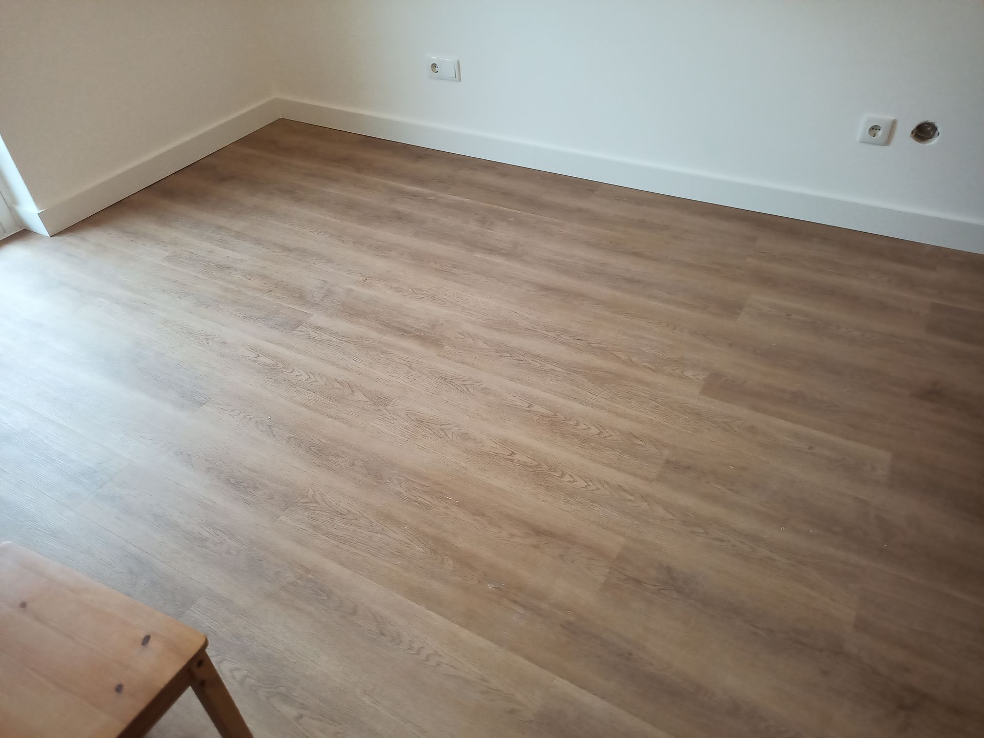 Piso laminado marrom claro em um cômodo vazio com paredes e rodapé brancos.